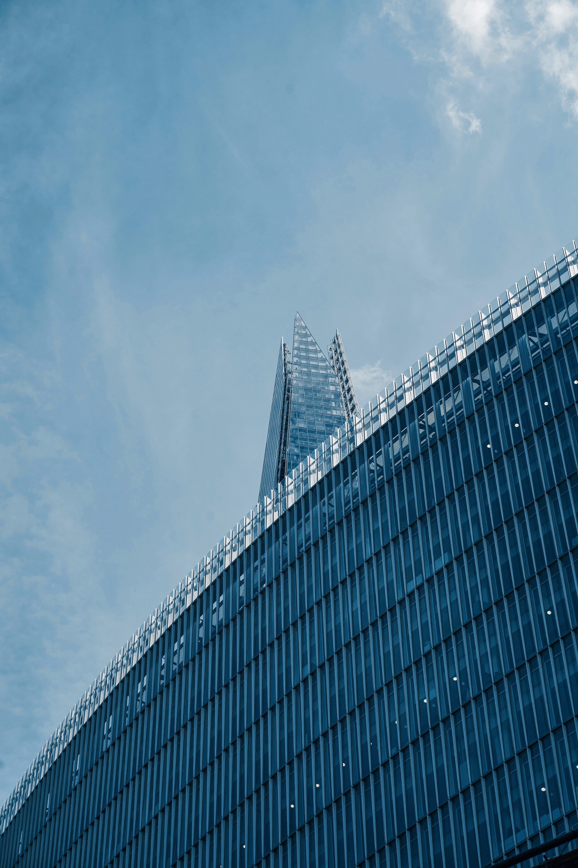 Angular building with a glass facade and sharp architectural spire under a partly cloudy sky.