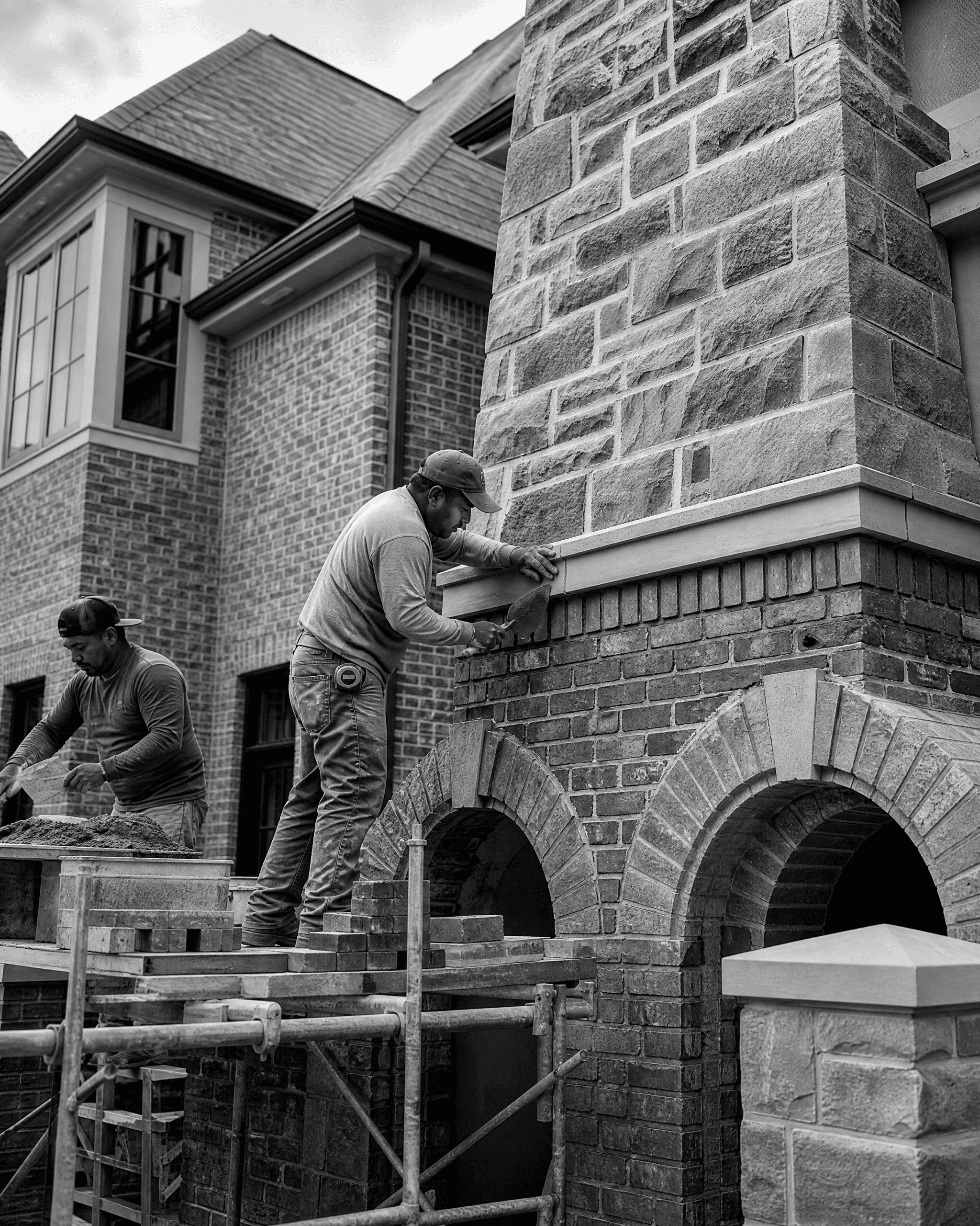 Masons working from scaffolding on a brick and stone exterior architectural feature.