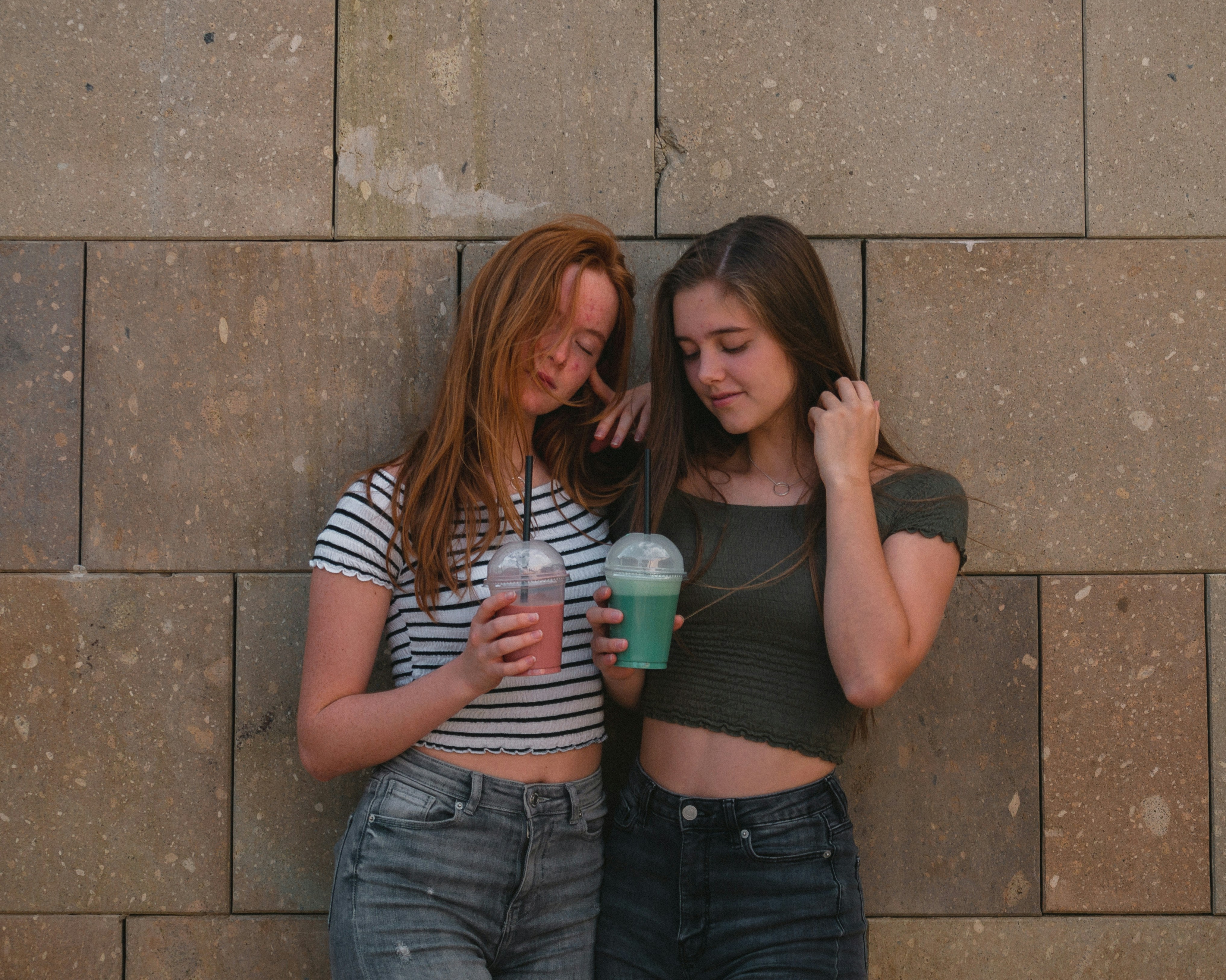 two women leaning on gray wall