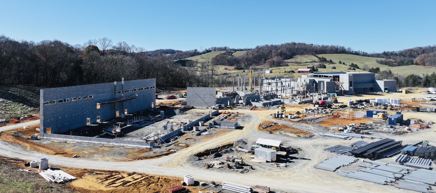 Aerial view of a construction site with multiple buildings and machinery, surrounded by a natural landscape.