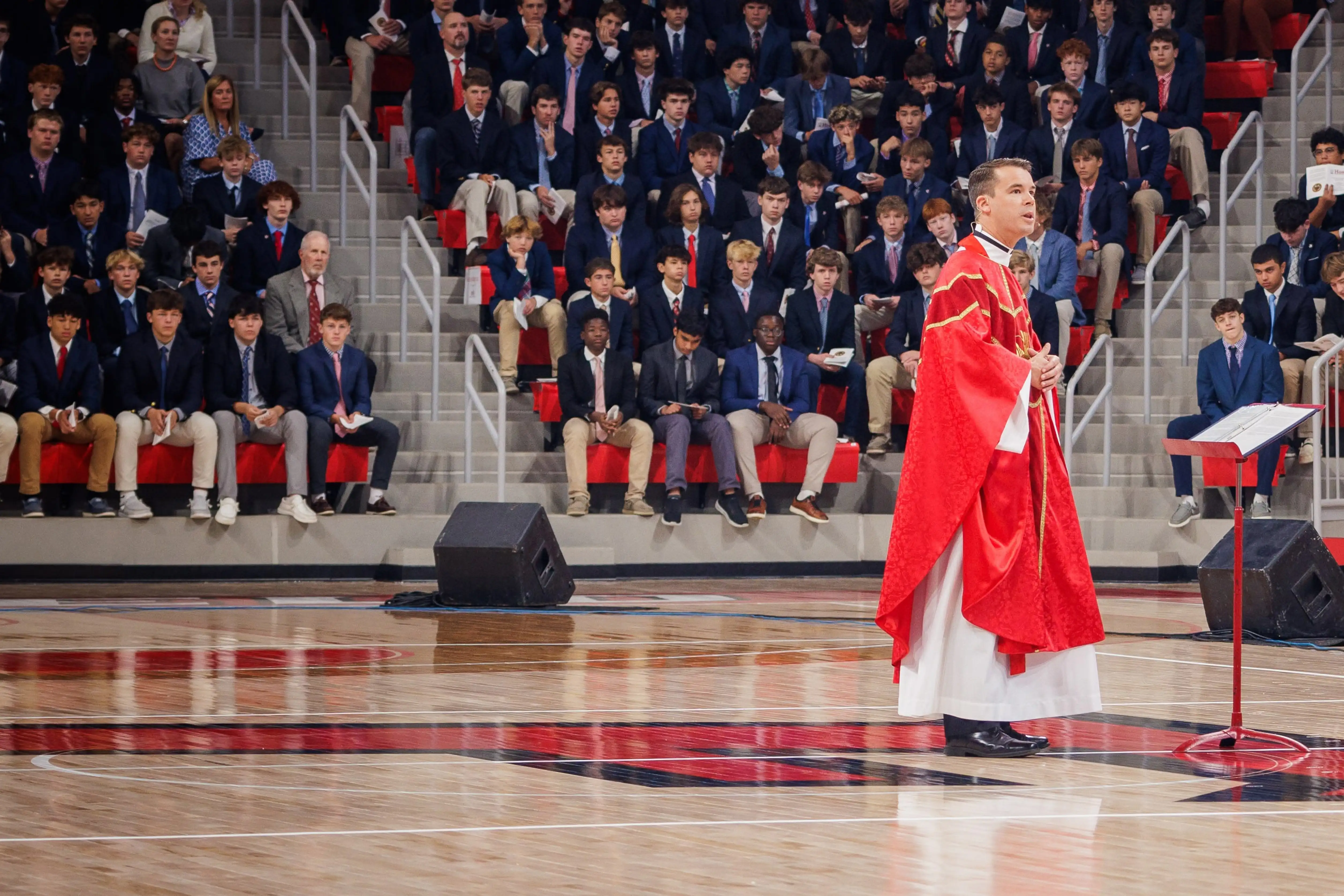 A performer in a red outfit dances on a basketball court, with an audience in the background.