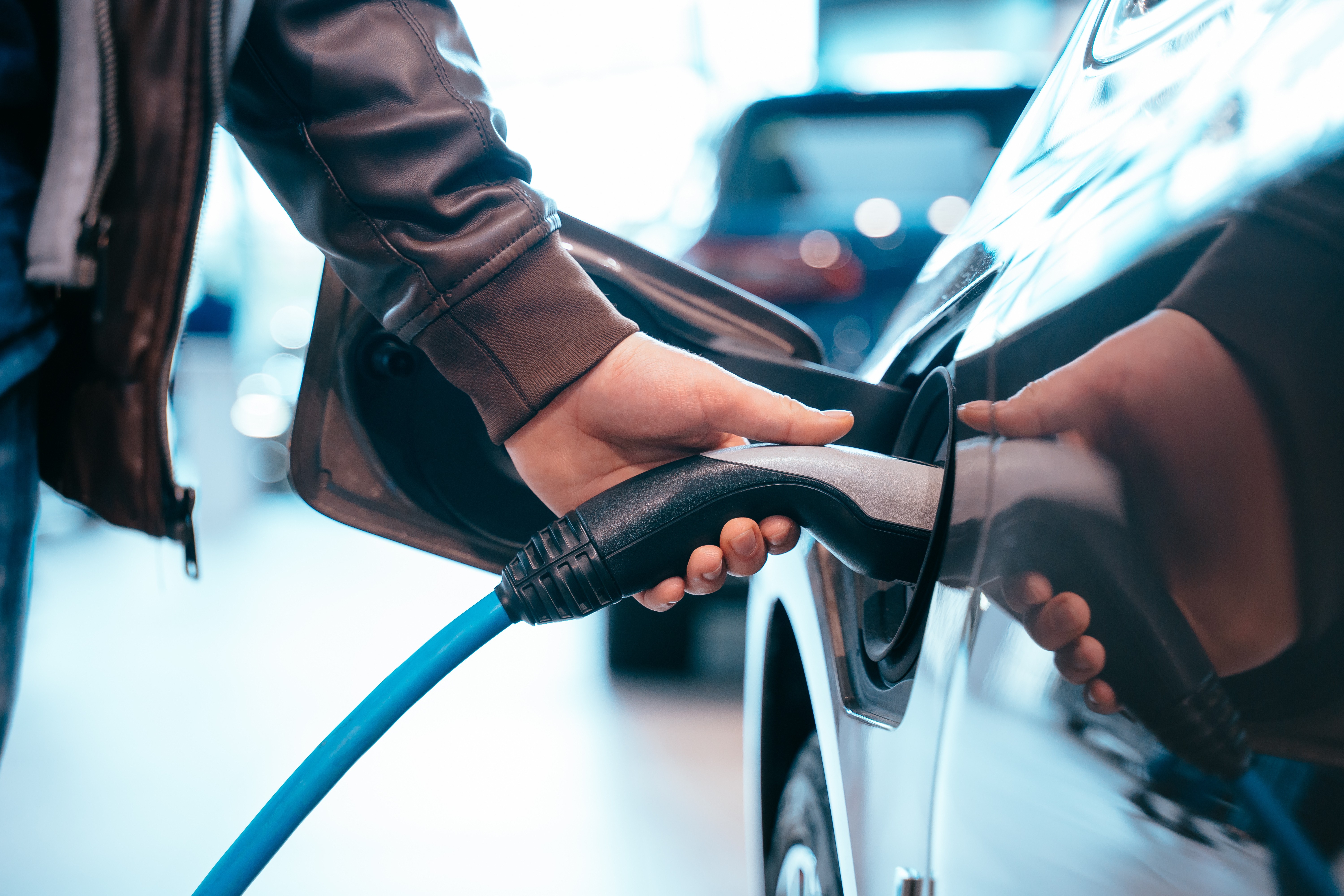 Person plugging a blue charging cable into the charging port of a white electric car