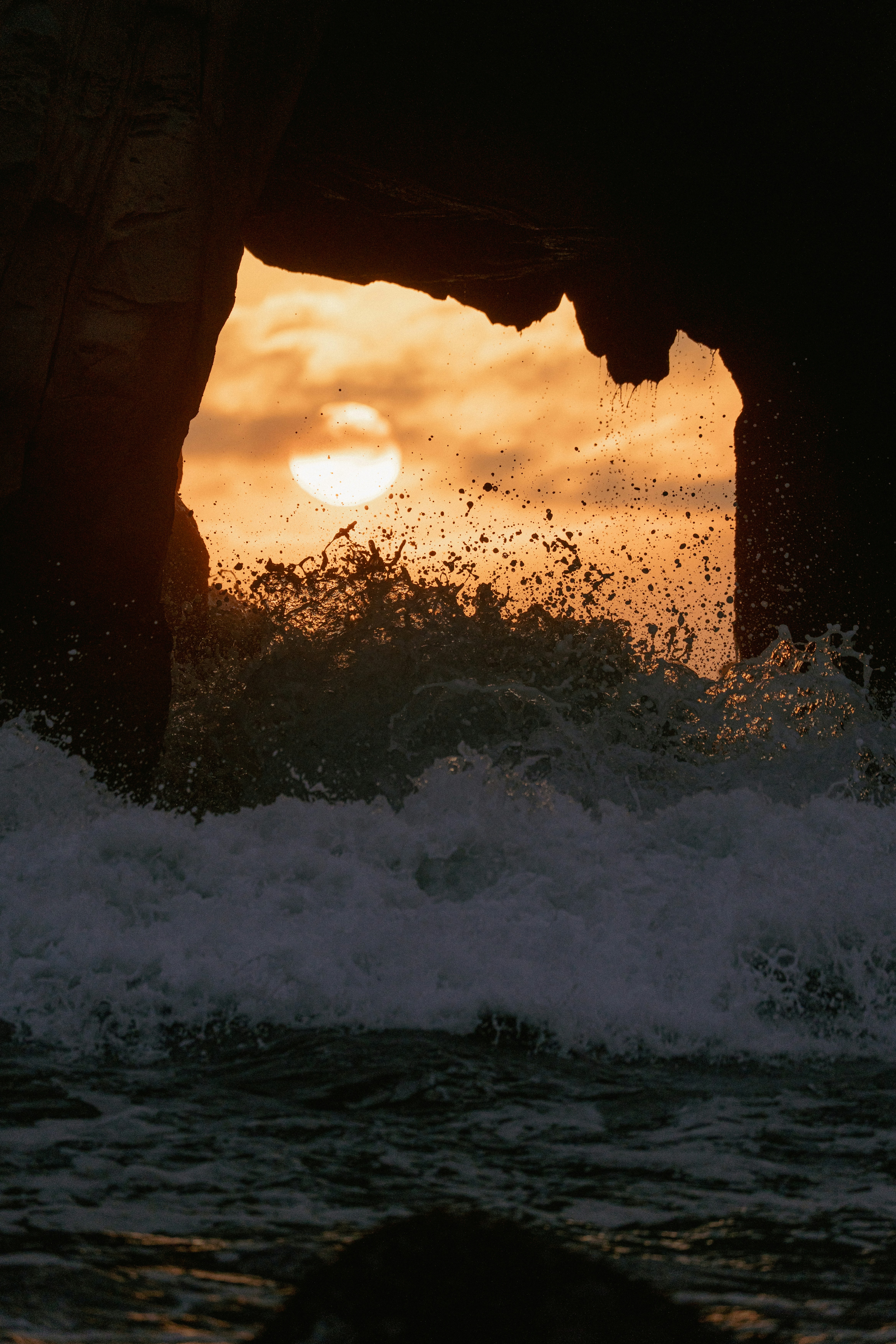Sunset viewed through a rock arch with ocean waves crashing.