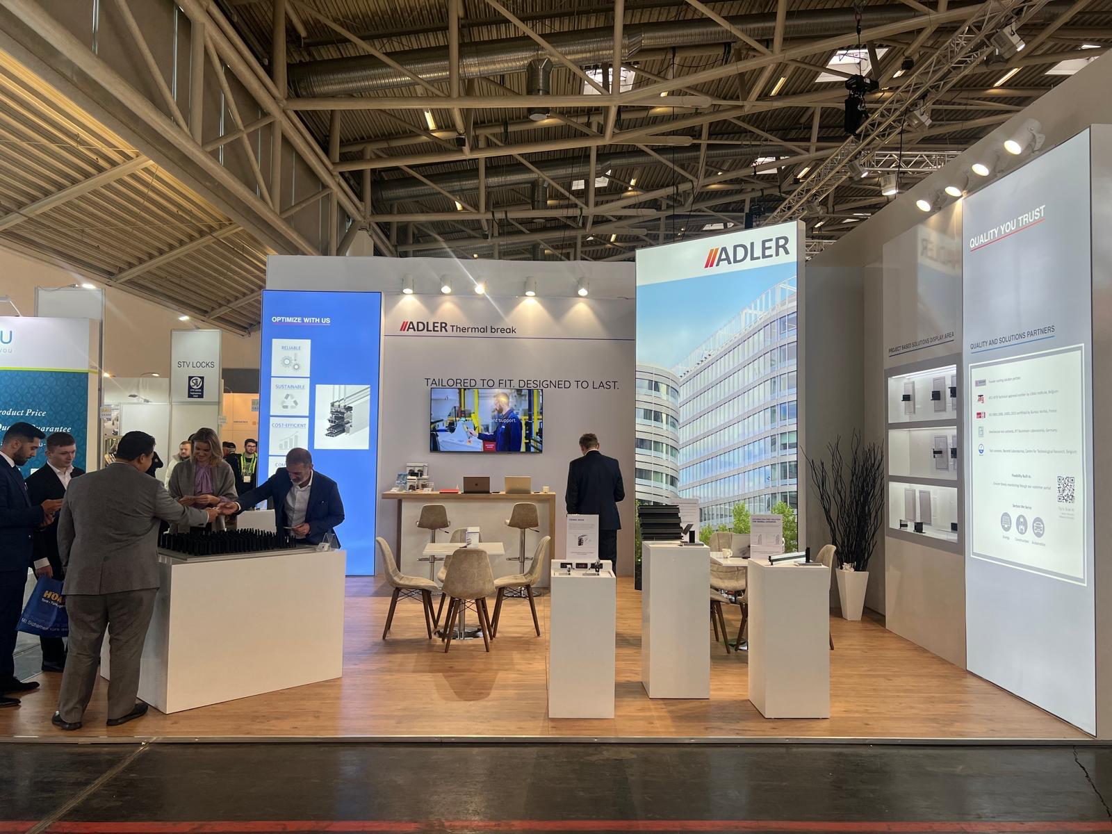 Large illuminated graphics and digital screens at the Adler stand, communicating product benefits such as reliability, sustainability, and cost efficiency.