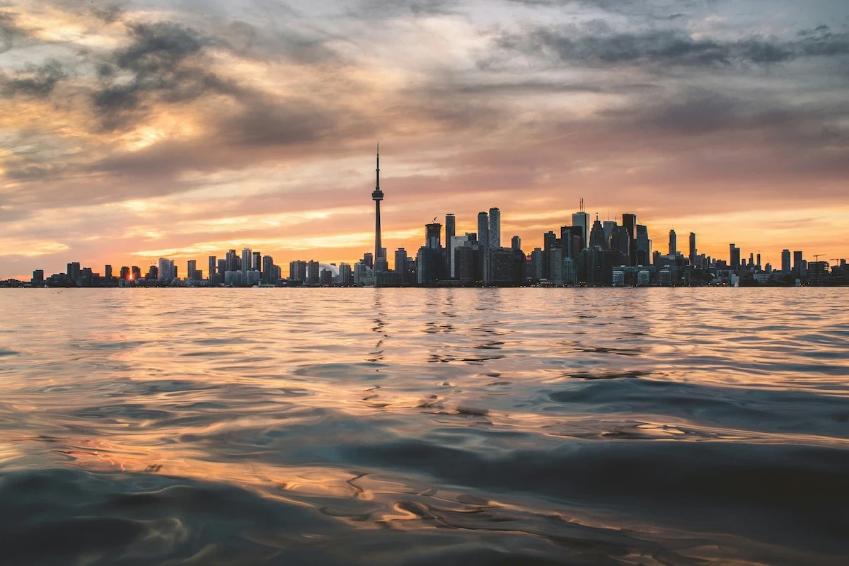 Toronto skyline at sunset with the CN Tower above Lake Ontario and orange light on the water.