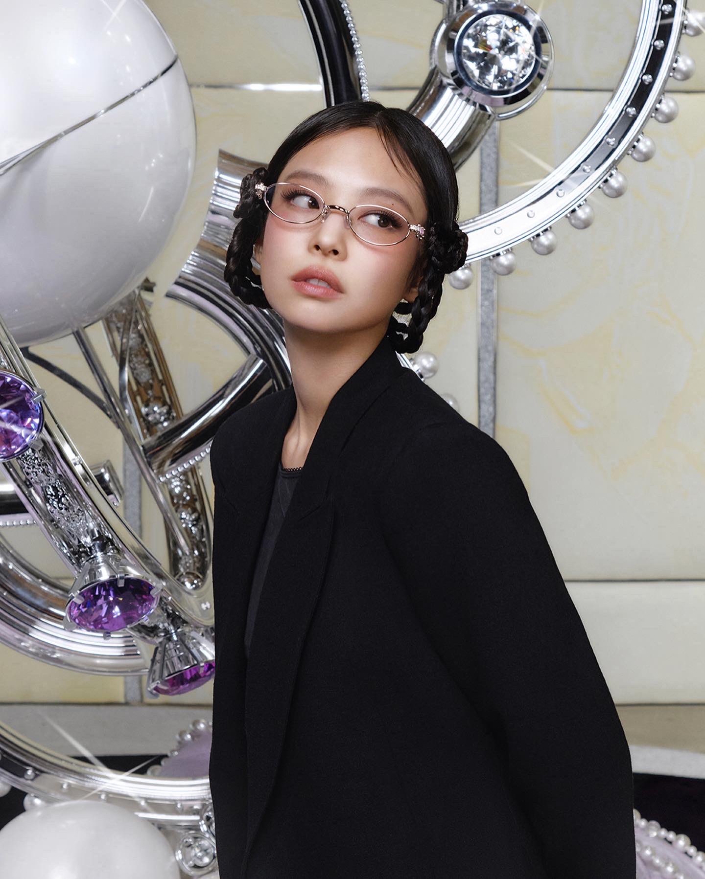 Jennie of K-pop group BLACKPINK wearing slim Gentle Monster glasses and a black blazer poses in front of a futuristic metallic installation with reflective spheres and crystal-like details.