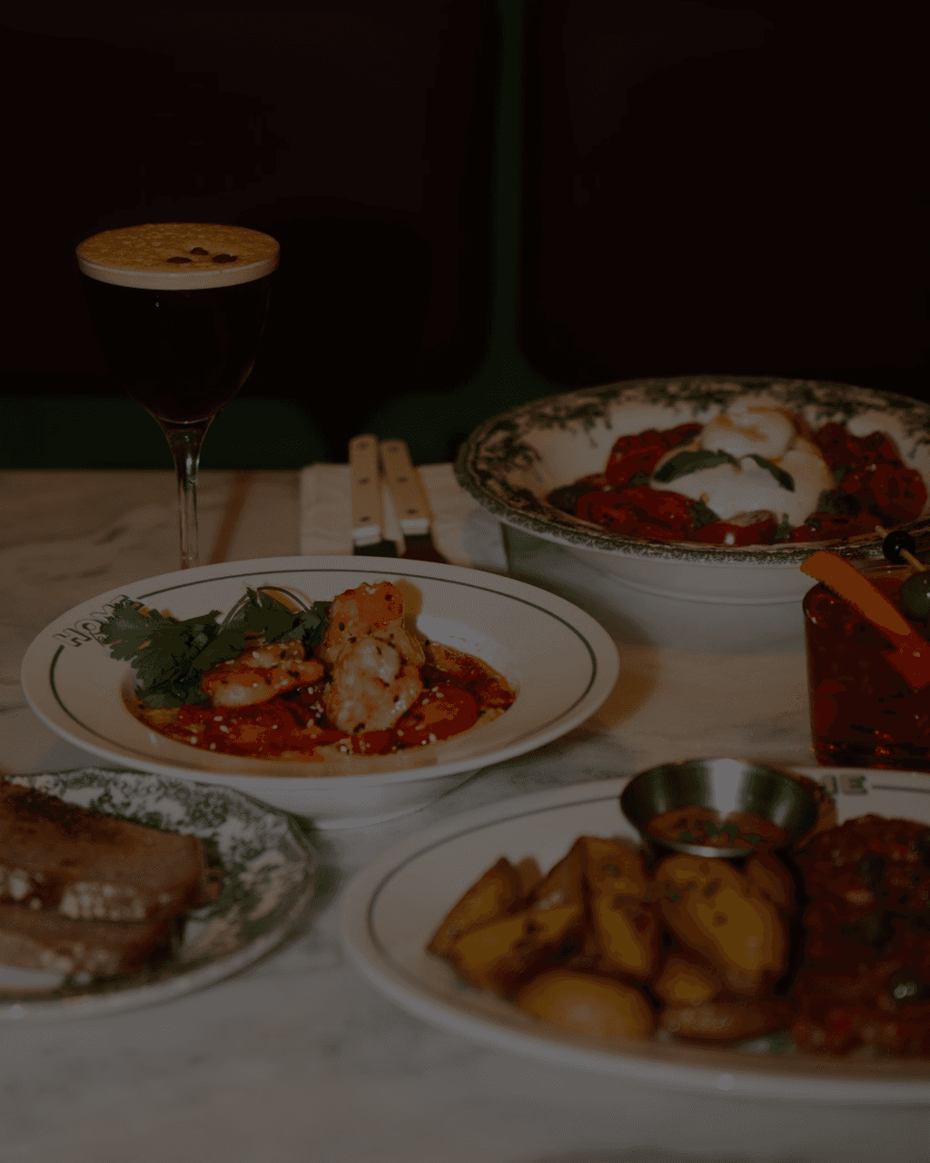 A smiling bartender in a dimly lit cafe shakes a cocktail mixer, surrounded by various coffee and beverage equipment.