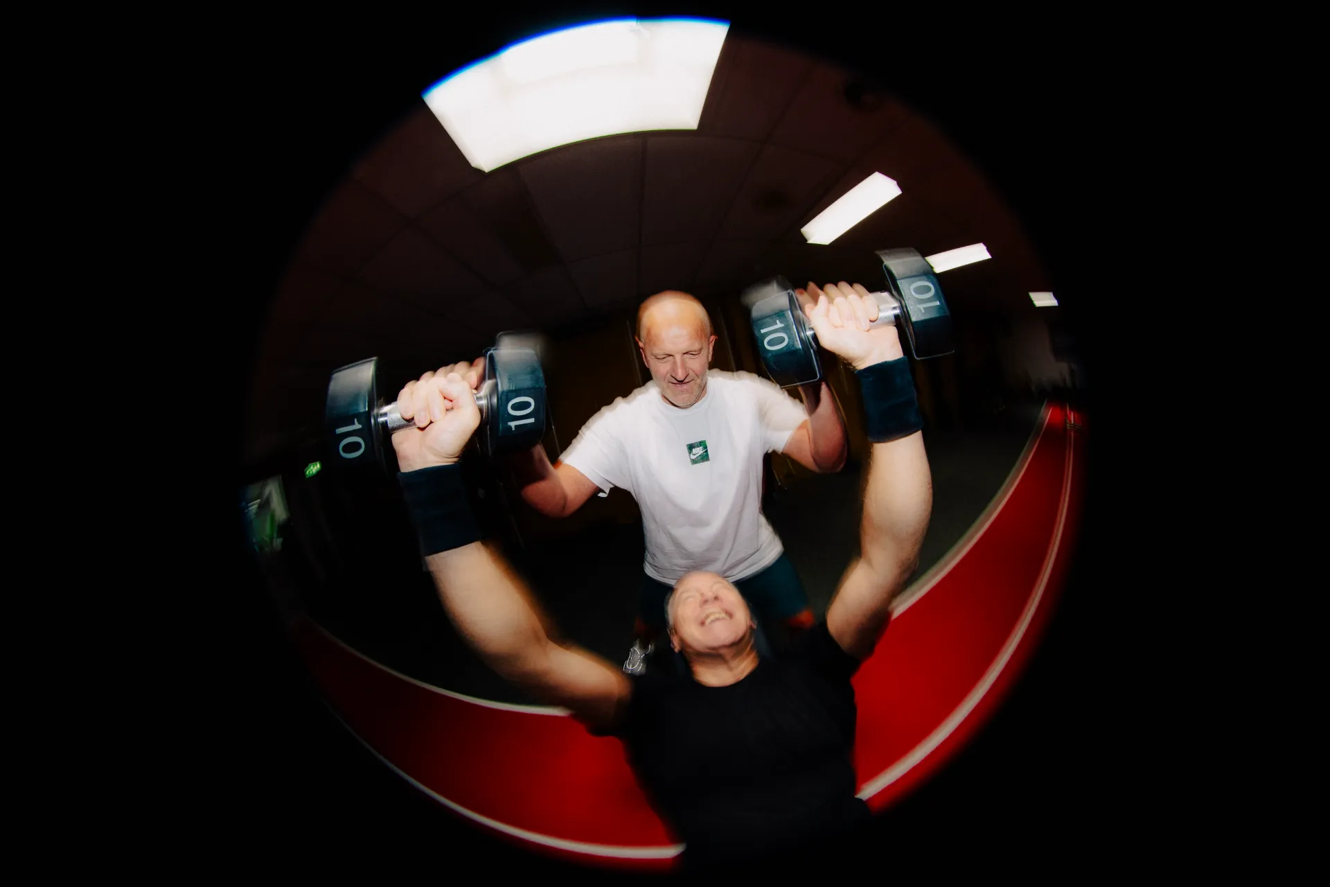 Twee sporters trainen met dumbbells terwijl de coach meekijkt
