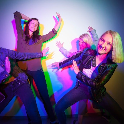 Четирима души приемат закачливи пози до стена с цветни сенки, хвърляни от разноцветни светлини.