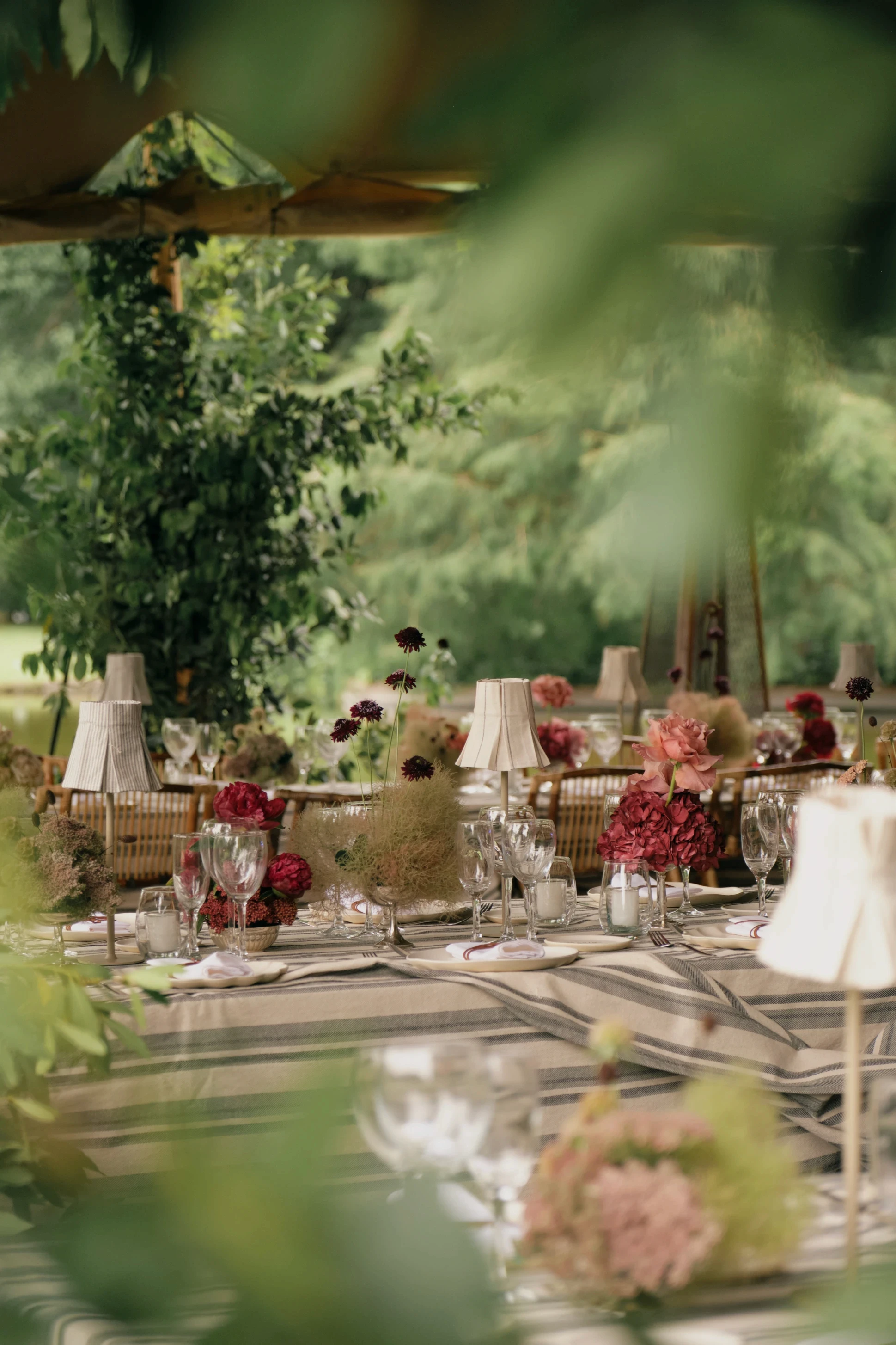 Vista de una mesa larga de recepción con arreglos florales en tonos fucsia y rosa bajo una carpa tensada.