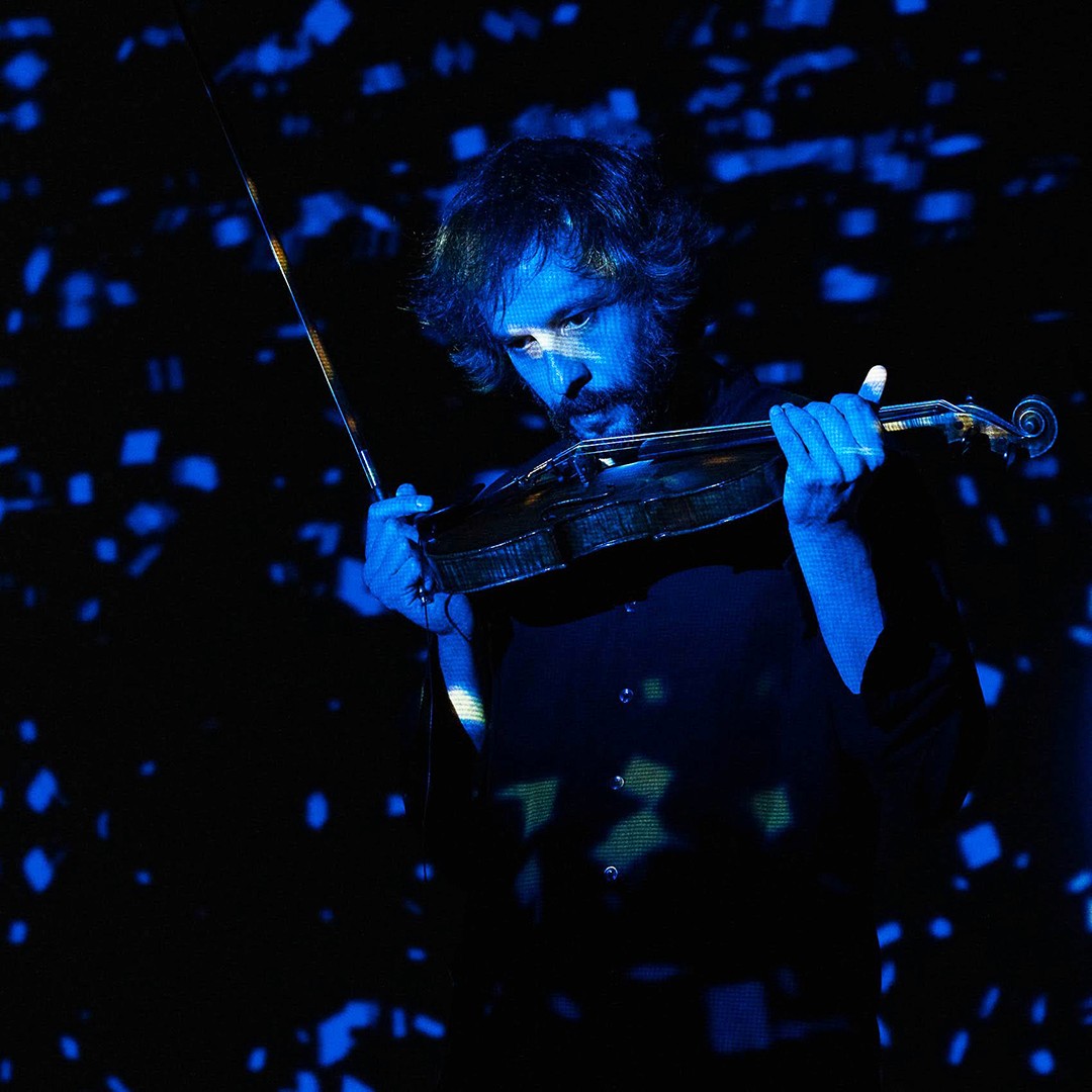 Man blowing the strings of a violin with blue digital texture projected on it.