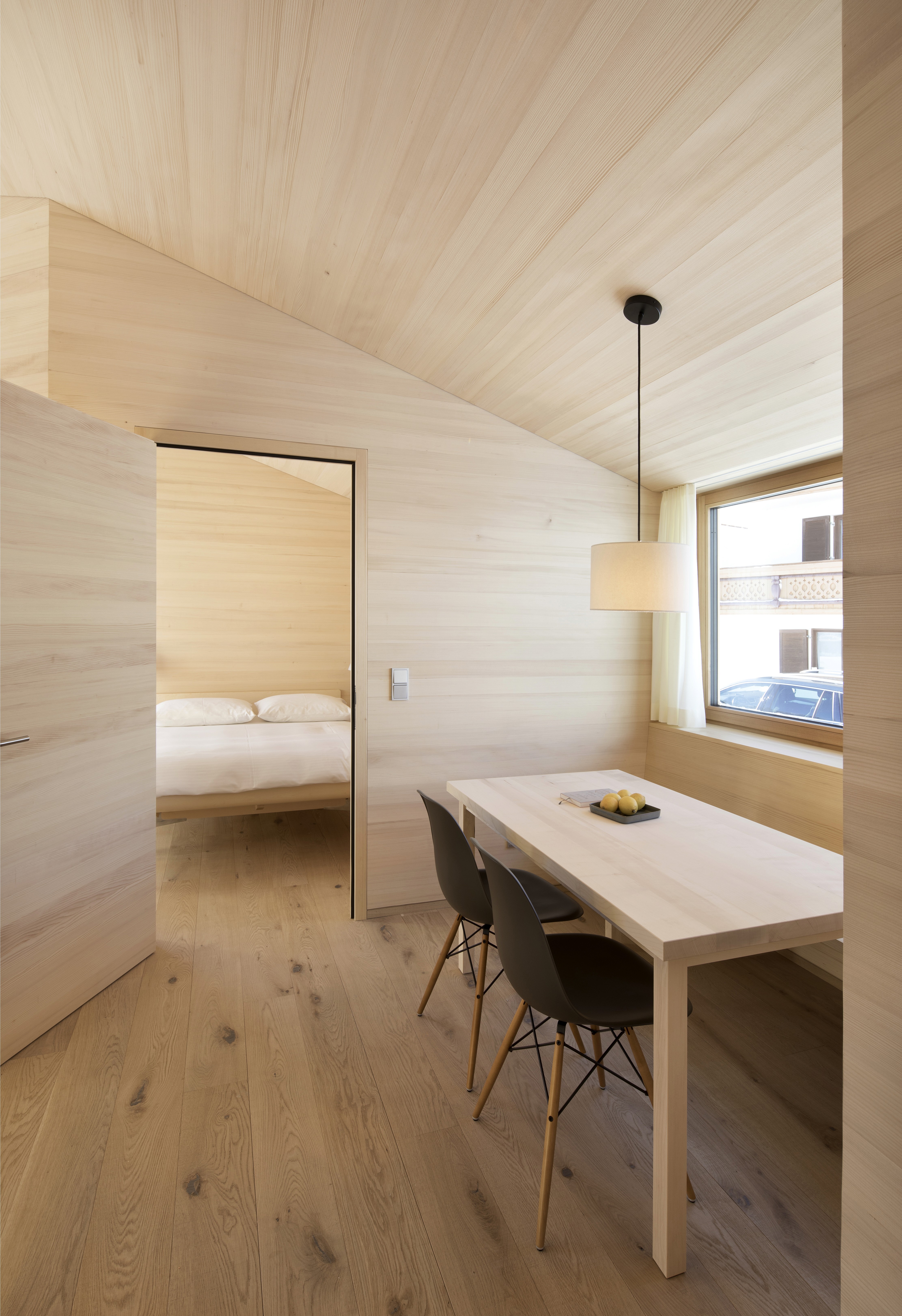 Bright wooden dining area with a simple table and chairs, leading into a bedroom with minimalist alpine design