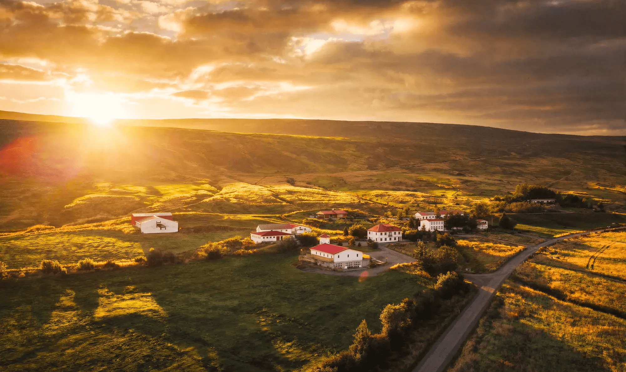 Aerial view of Aurora Farm Hotel's cluster of red-roofed farm buildings at sunset