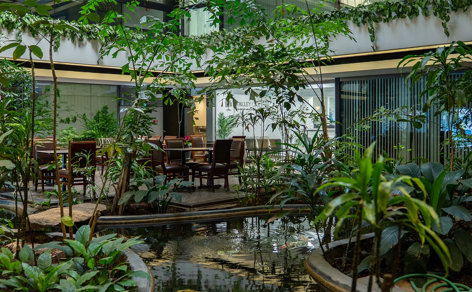 Indoor garden courtyard at Valley Oak Oral Surgery featuring lush greenery, natural light, and a modern blue content panel highlighting patient-centered oral surgery care in Fresno, CA.