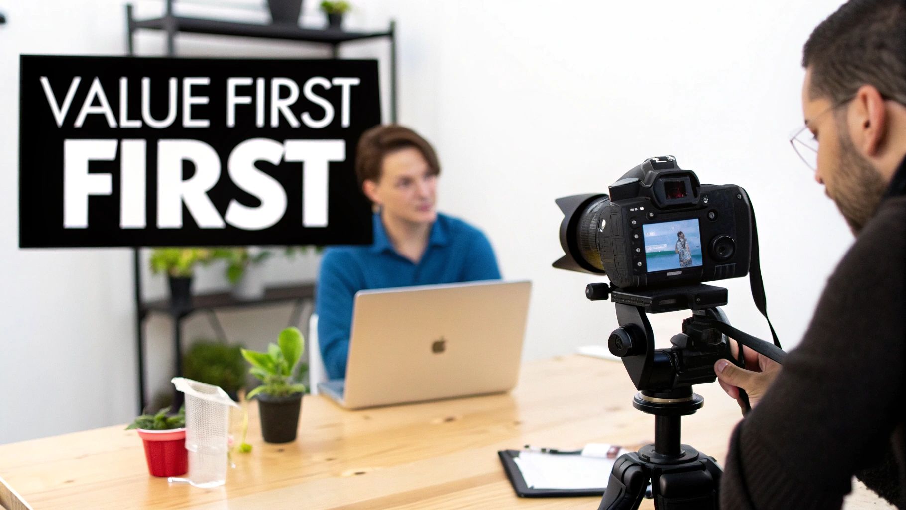 A person films another individual presenting 'VALUE FIRST' on a laptop in a modern studio setting.