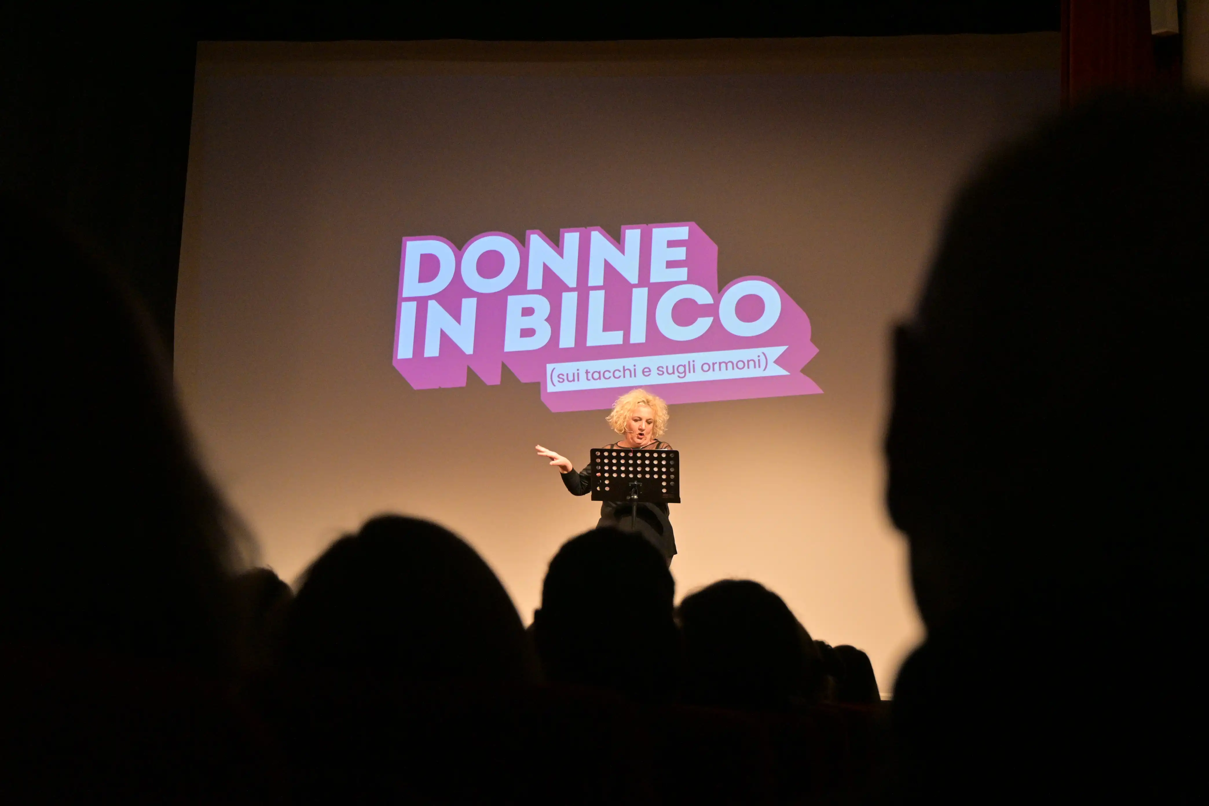 Maria Pia Timo sul palco del teatro verdi di Forlimpopoli con logo Donne in Bilico proiettato a schermo