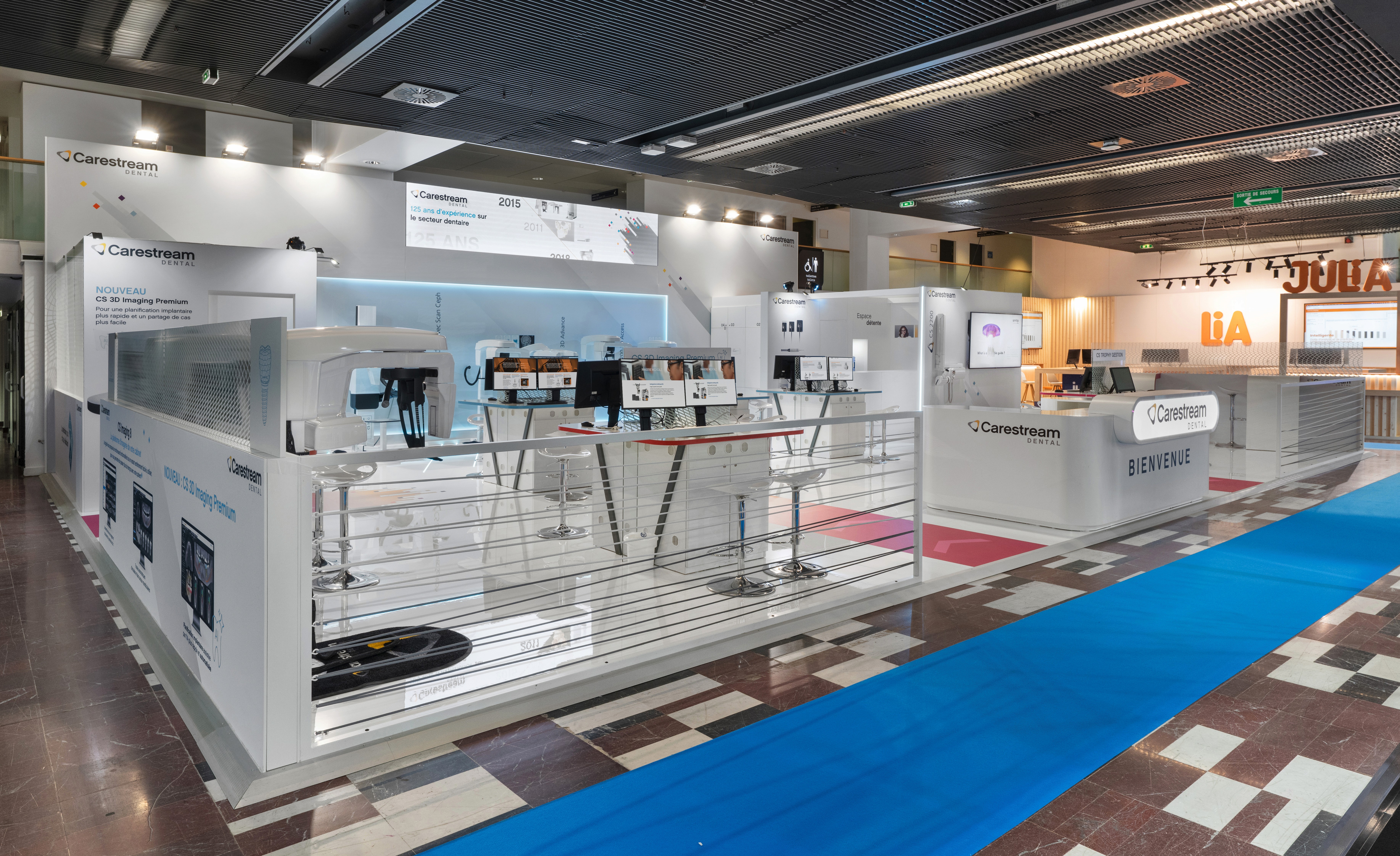 Stand Carestream Dental congrès ADF conçu par Expace – vue extérieure avec structure surélevée, comptoir d'accueil Bienvenue, zone démonstration CS 3D Imaging Premium et frise historique de la marque