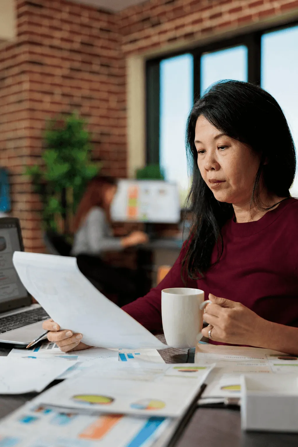 Person writing at a desk with papers and cups.