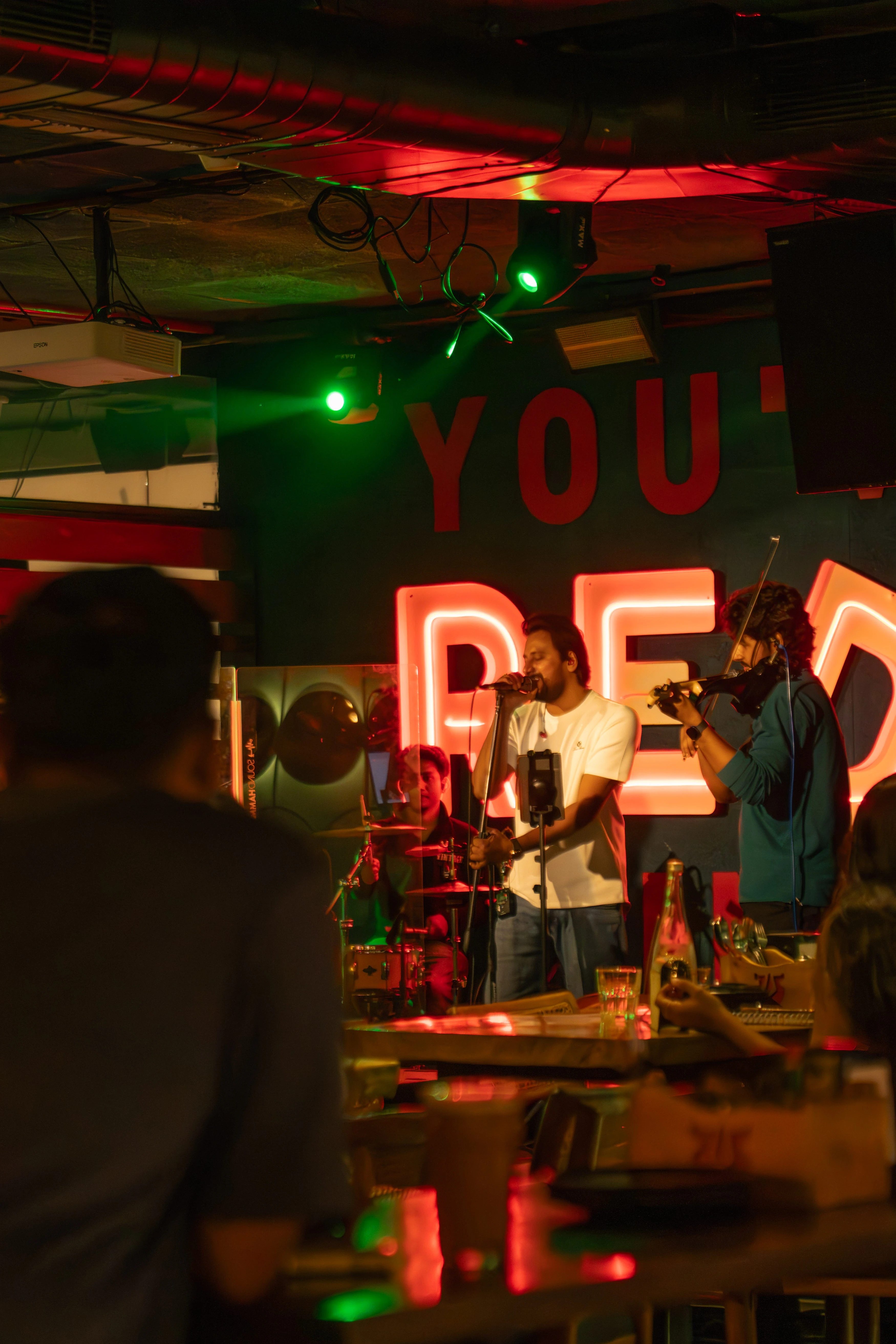 Live music performance at Red Rhino craft brewery featuring singer and violinist on stage with neon red lighting and guests enjoying drinks.
