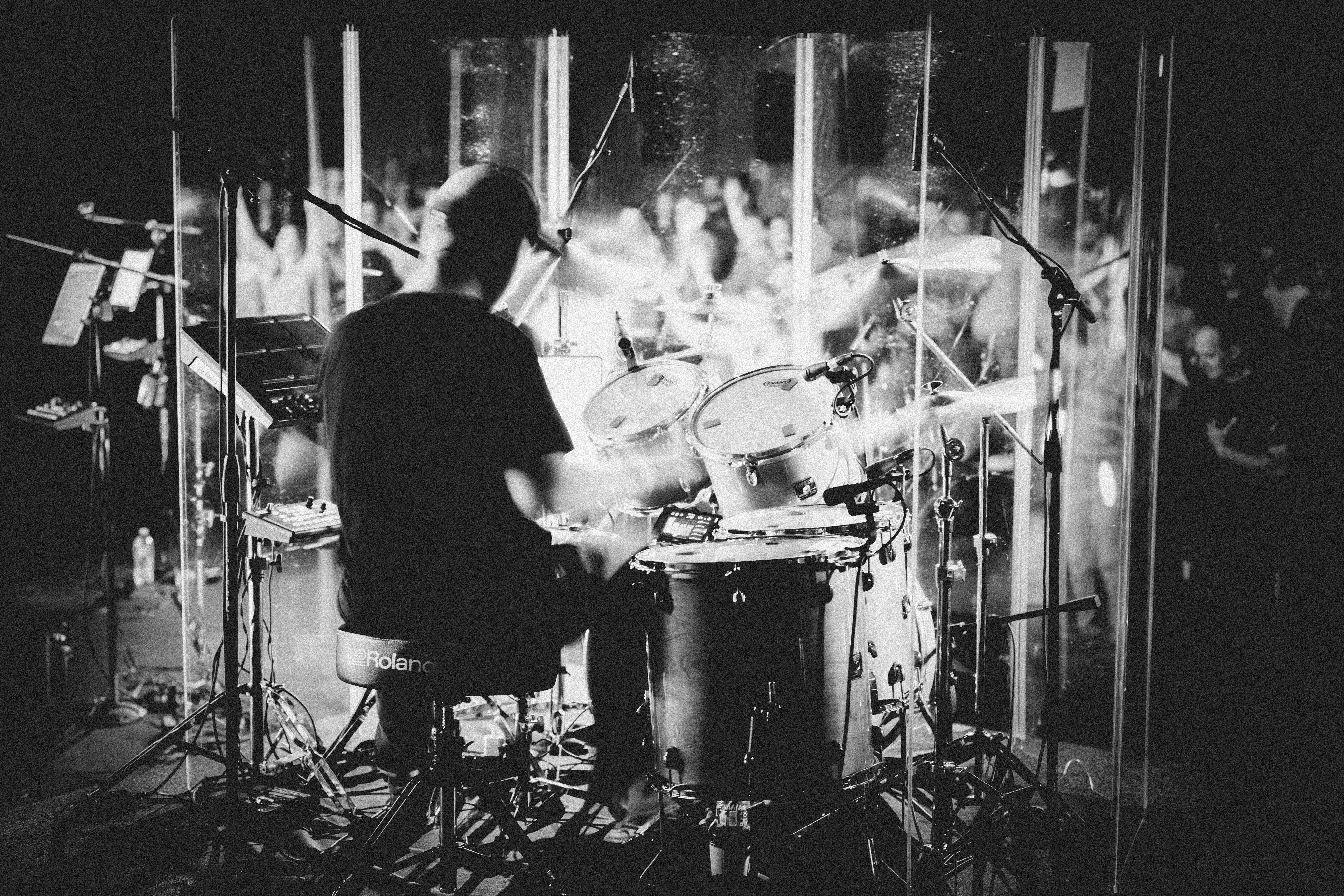 Man in black-and-white image playing drums in concert setting in front of audience