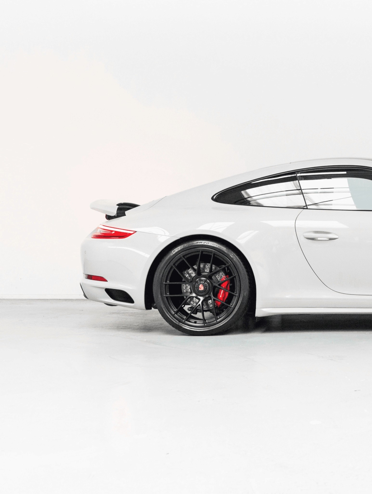A sleek white sports car with a streamlined design is parked in a minimalist indoor setting, showcasing its glossy finish, black alloy wheels, and distinctive rear spoiler, ideal for luxury car enthusiasts.