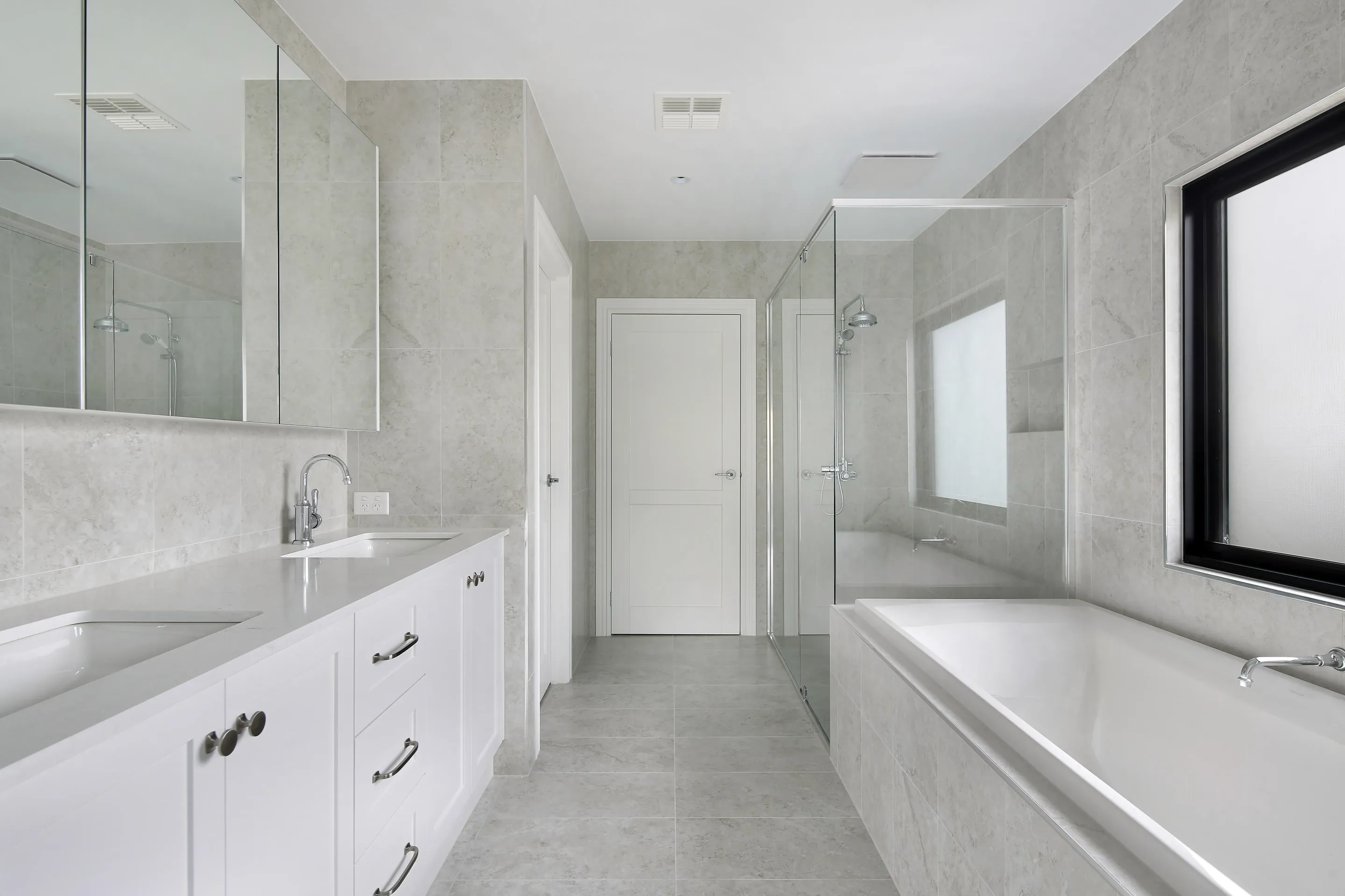 Main bathroom with a white shaker double vanity, mirrored cabinets, a built-in bath, a glass shower, frosted black-framed window and grey stone-look tiles