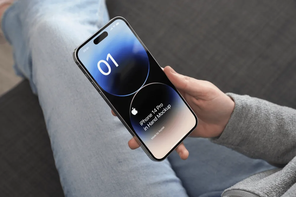 A person holding an iPhone 14 Pro displaying a minimalistic dark interface with blue and black tones, seated on a gray couch wearing light jeans and a gray sweatshirt.