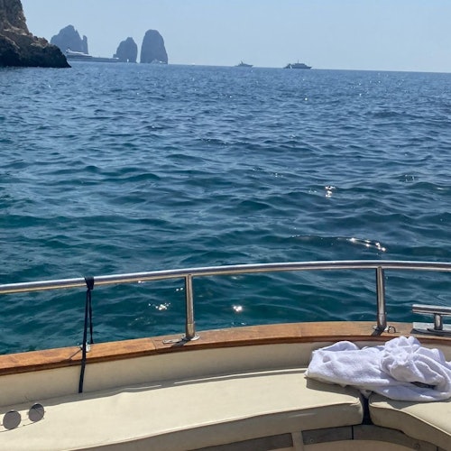 View from a boat’s cushioned deck looking out at the ocean, with cliffs and rock formations in the distance.