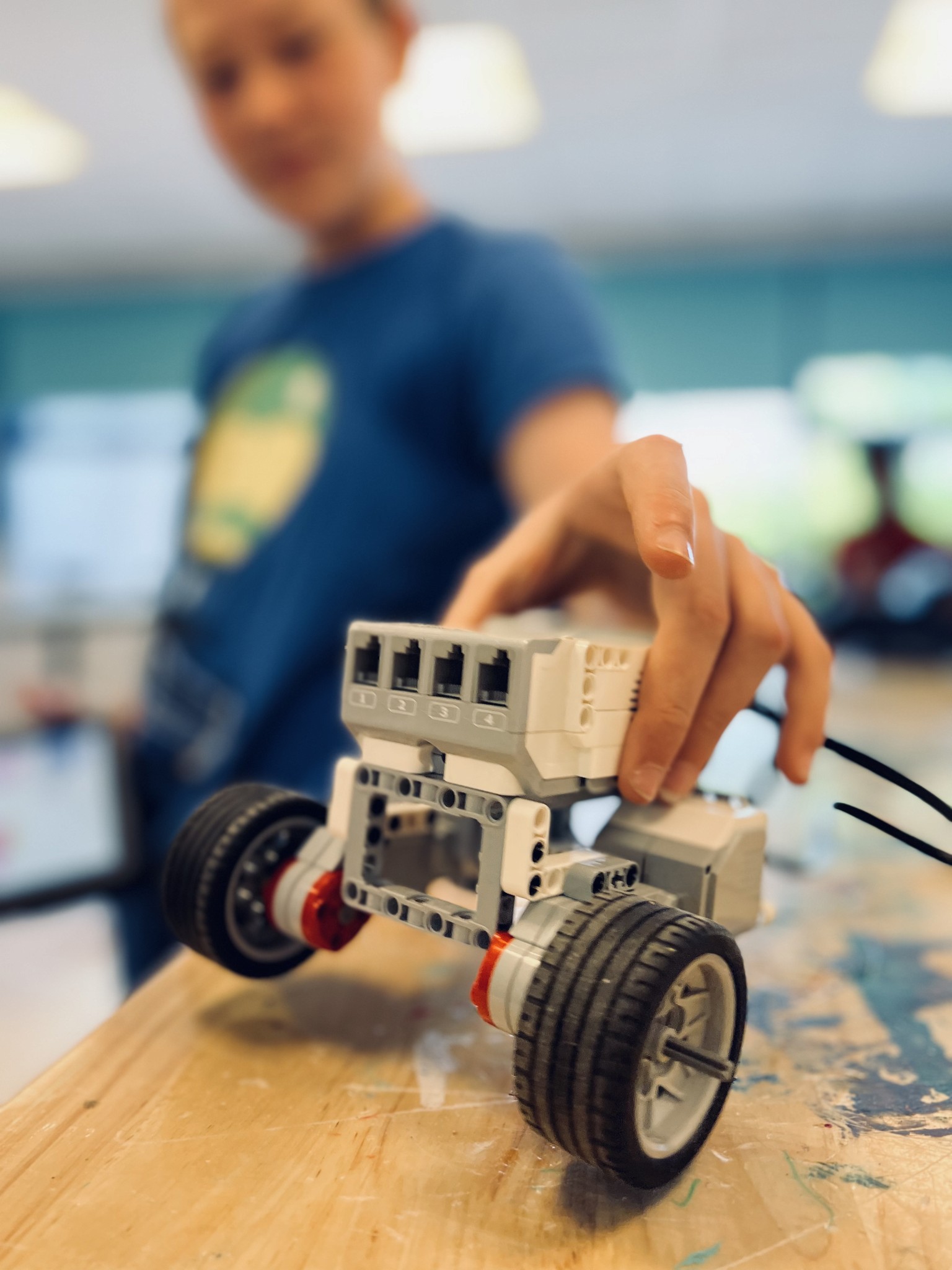 Child guiding a self-built LEGO Mindstorms robot car on a workbench during a robotics class