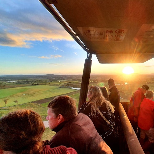 Mensen in een heteluchtballonmand genieten van het uitzicht op een uitgestrekt groen landschap tijdens zonsondergang.