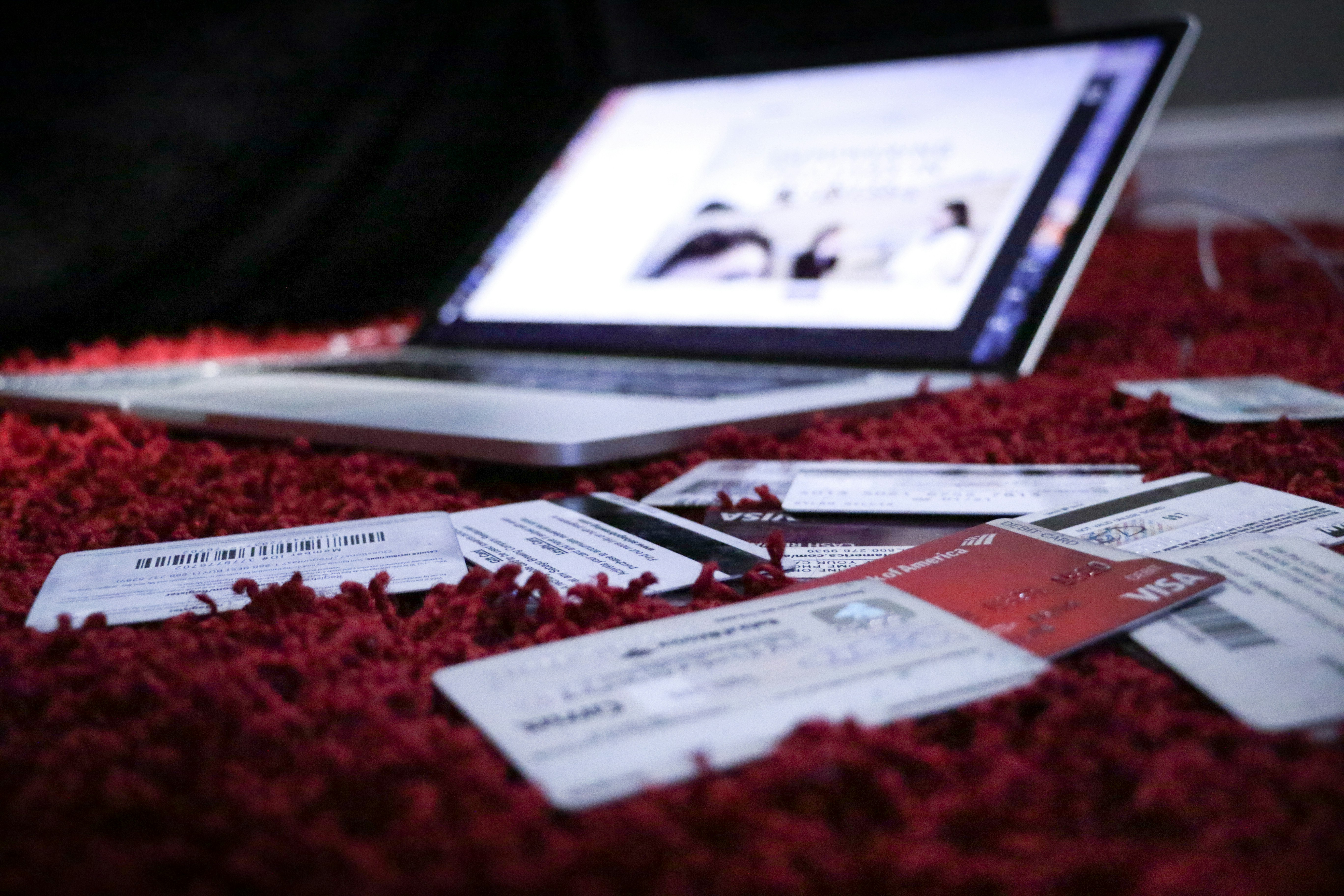 An open laptop with credit cards scattered around on a red blanket. 