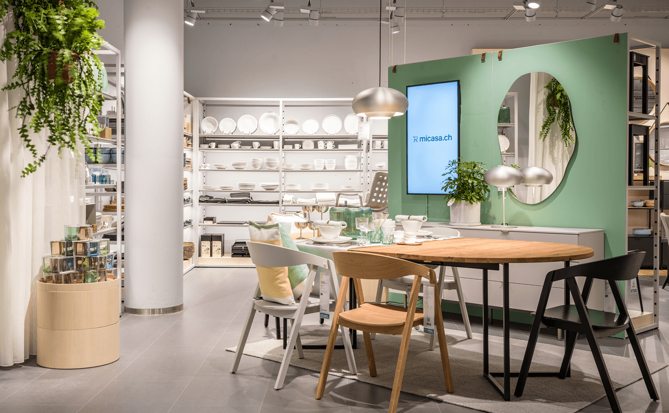 Blick in den micasa Experience Store mit modularen Regalmodulen als Raumtrenner, wandmontierten Regalen und Holztonnen zur Warenpräsentation.