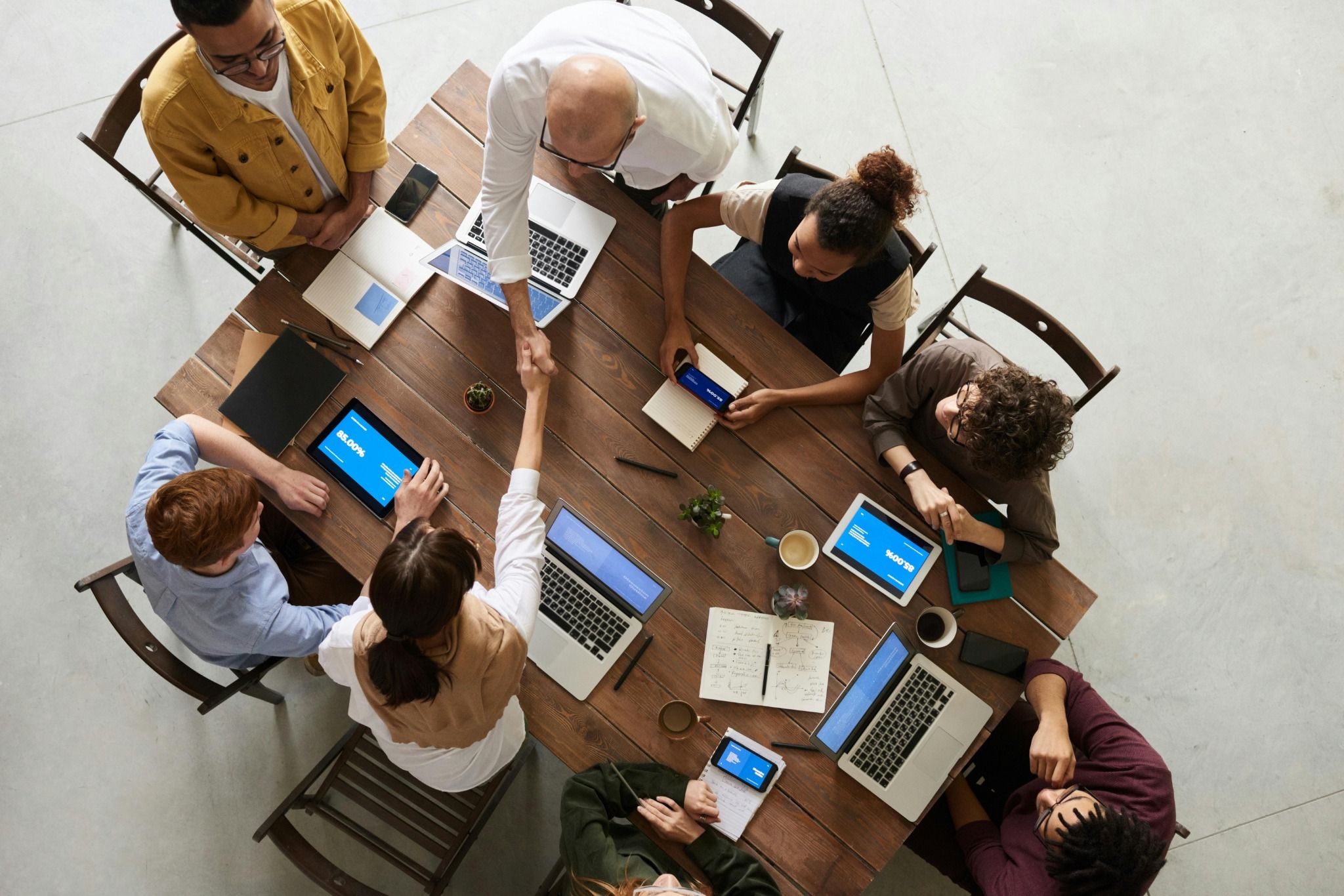 Team collaborating around a table with laptops and tablets showing the PatPat360 platform, with two people shaking hands.