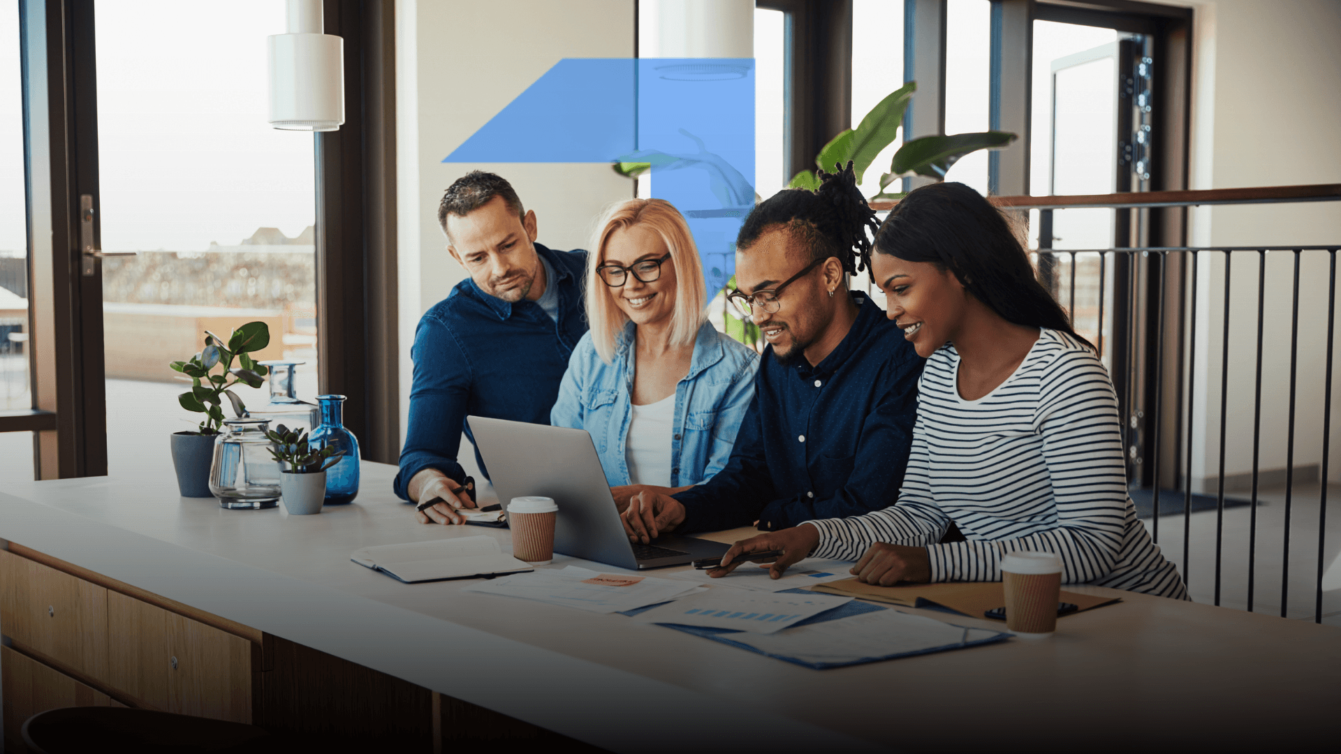 A group of four people, three men and one woman, sitting around a table and discussing something on a laptop working together