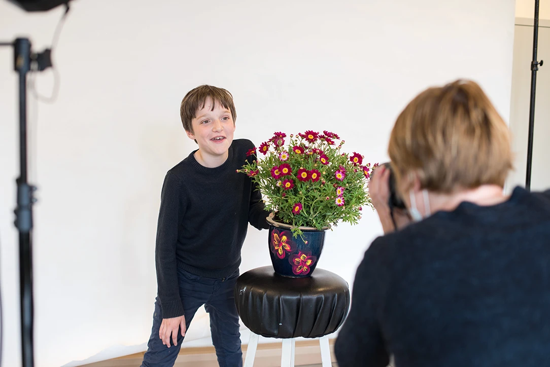 Jongen poseert lachend met een bloempot vol bloemen tijdens een fotoshoot