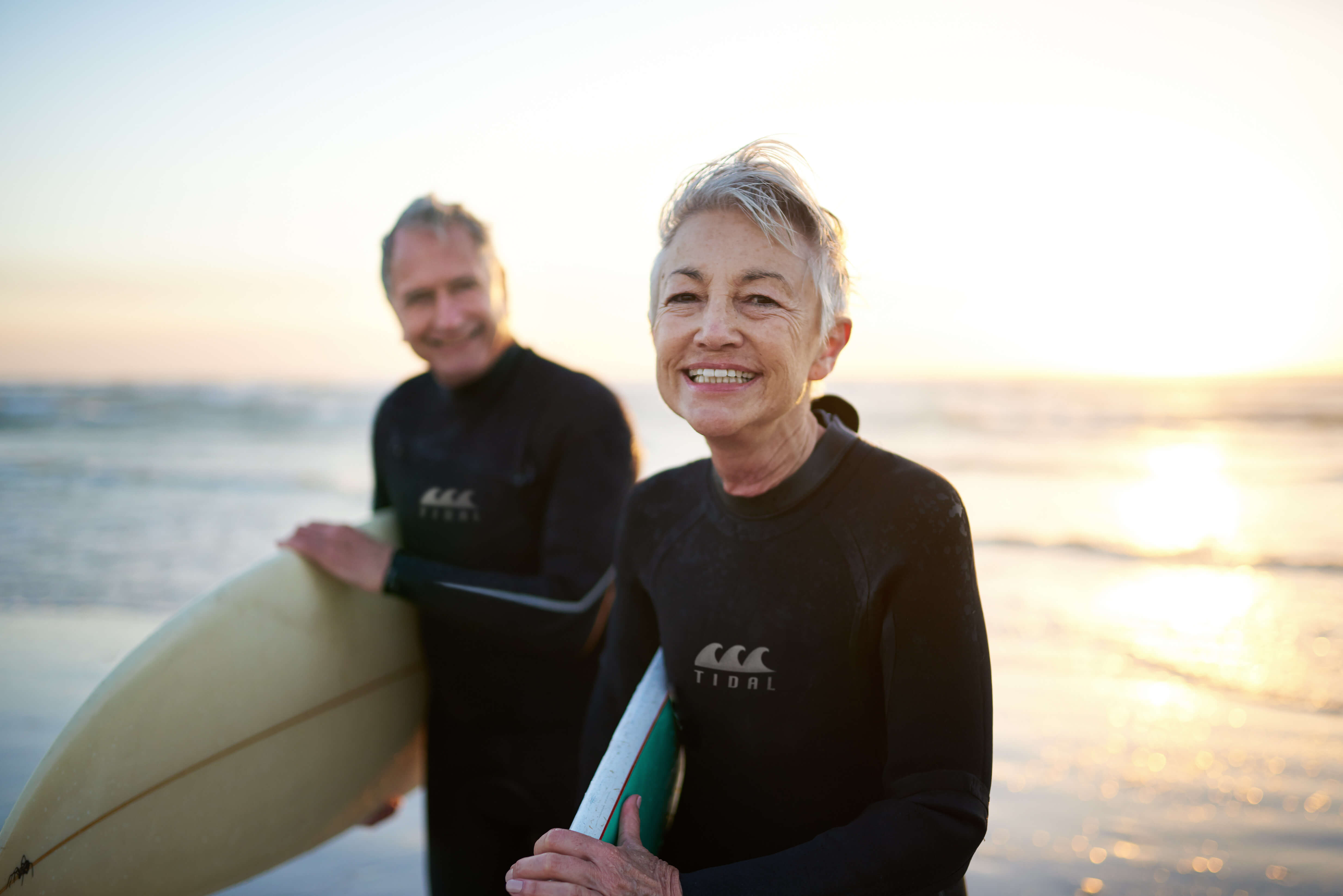 image of retired man and woman carrying surfboards