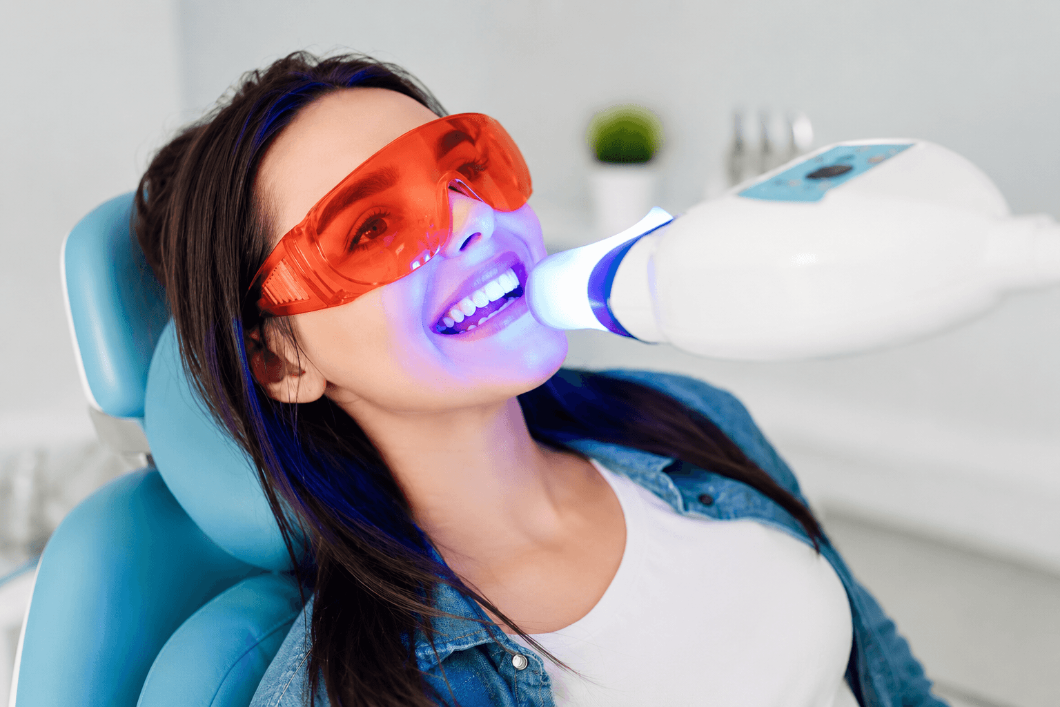Patientin während einer professionellen Zahnaufhellung mit Bleaching-Lampe und Schutzbrille in einer modernen Zahnarztpraxis in Karlsruhe.