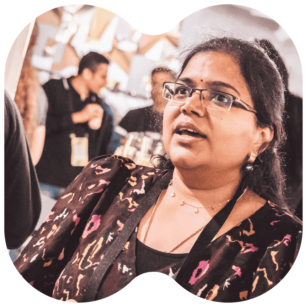 Person wearing a patterned top and lanyard in a busy event space with other attendees visible in the background.