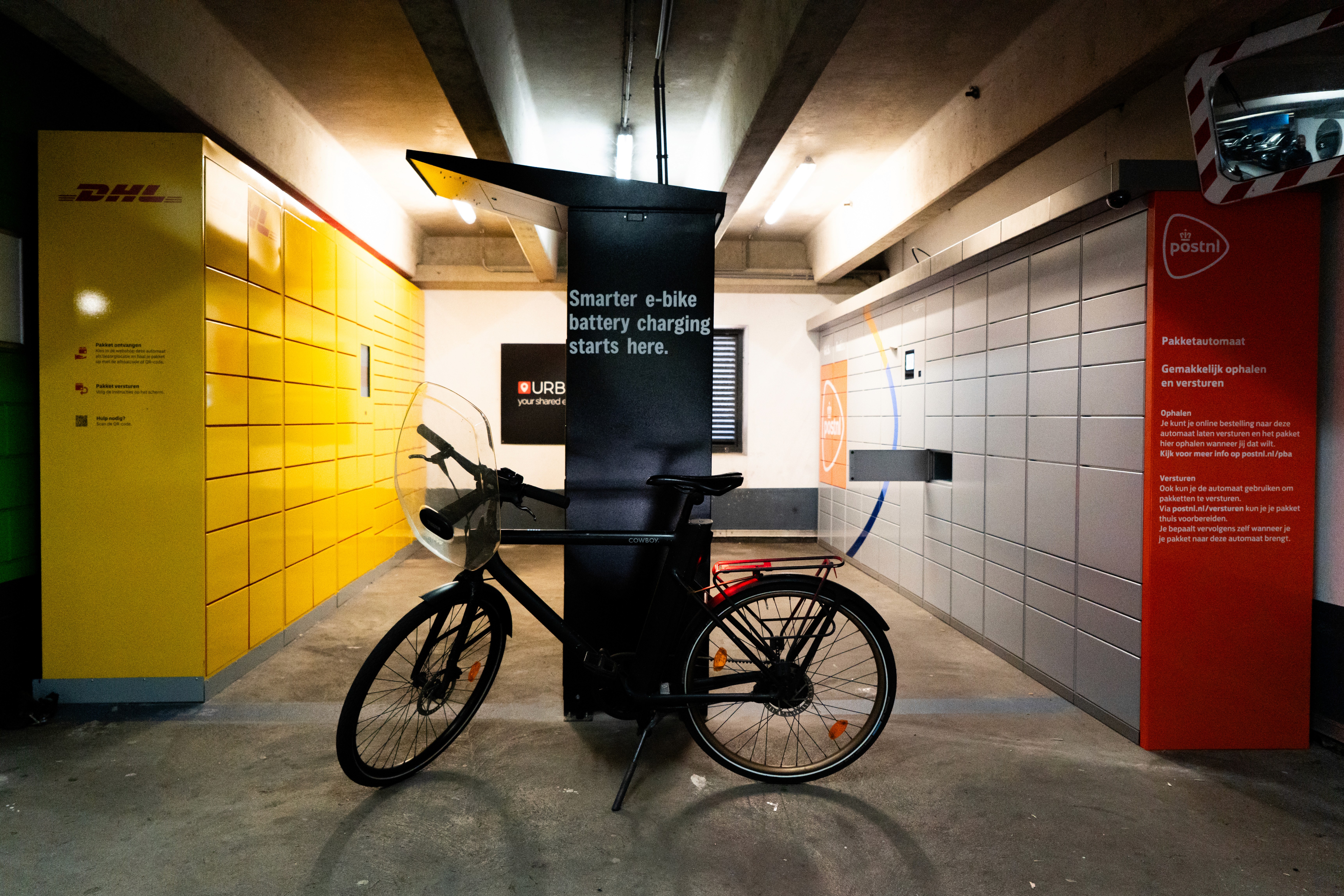 PowerShelter e-bike battery charging and swapping locker installed at APCOA Amsterdam, alongside DHL and PostNL parcel lockers.