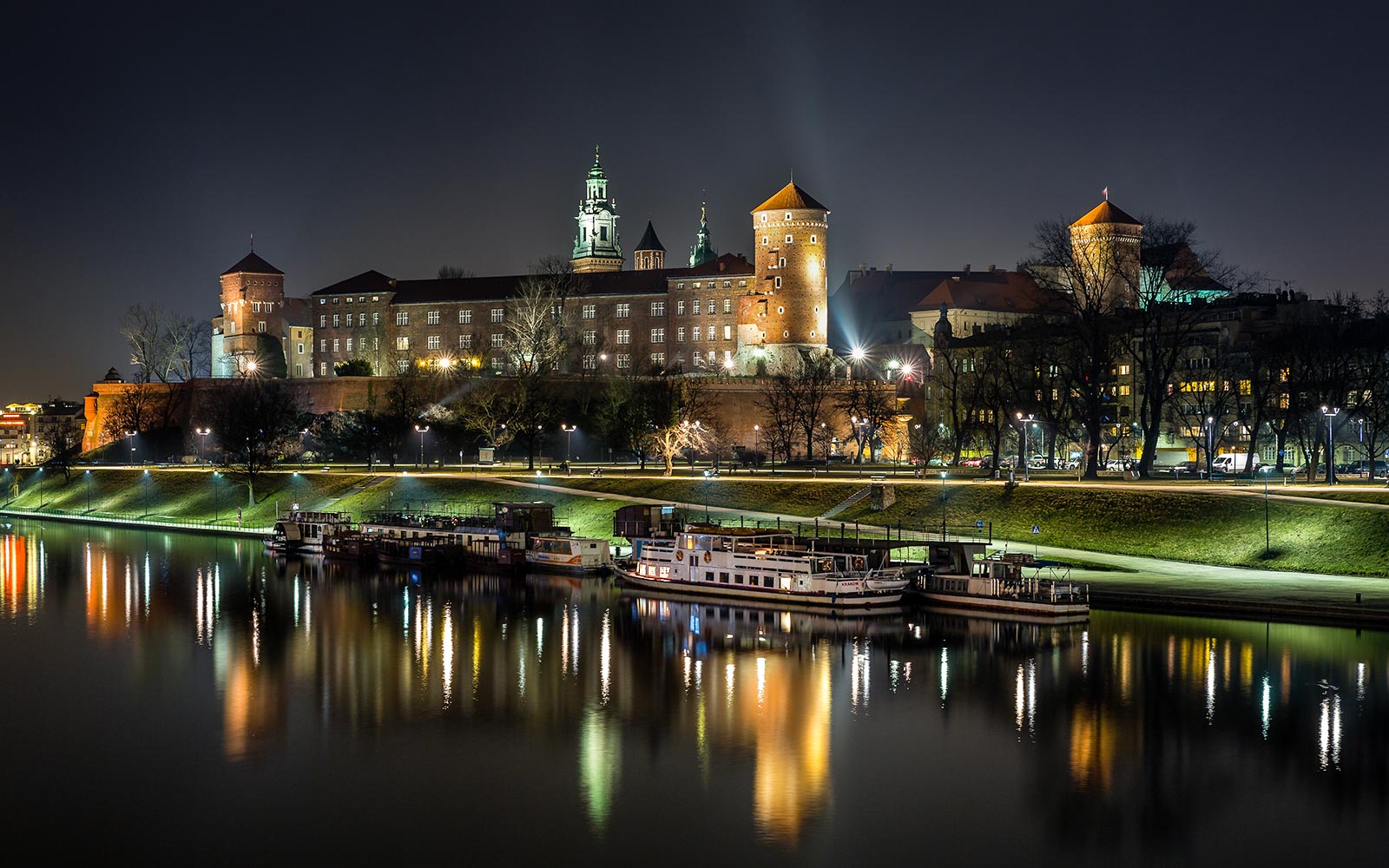 Wawel Castle illuminated at night, reflected in the Vistula River during a night cruise in Krakow, Poland.