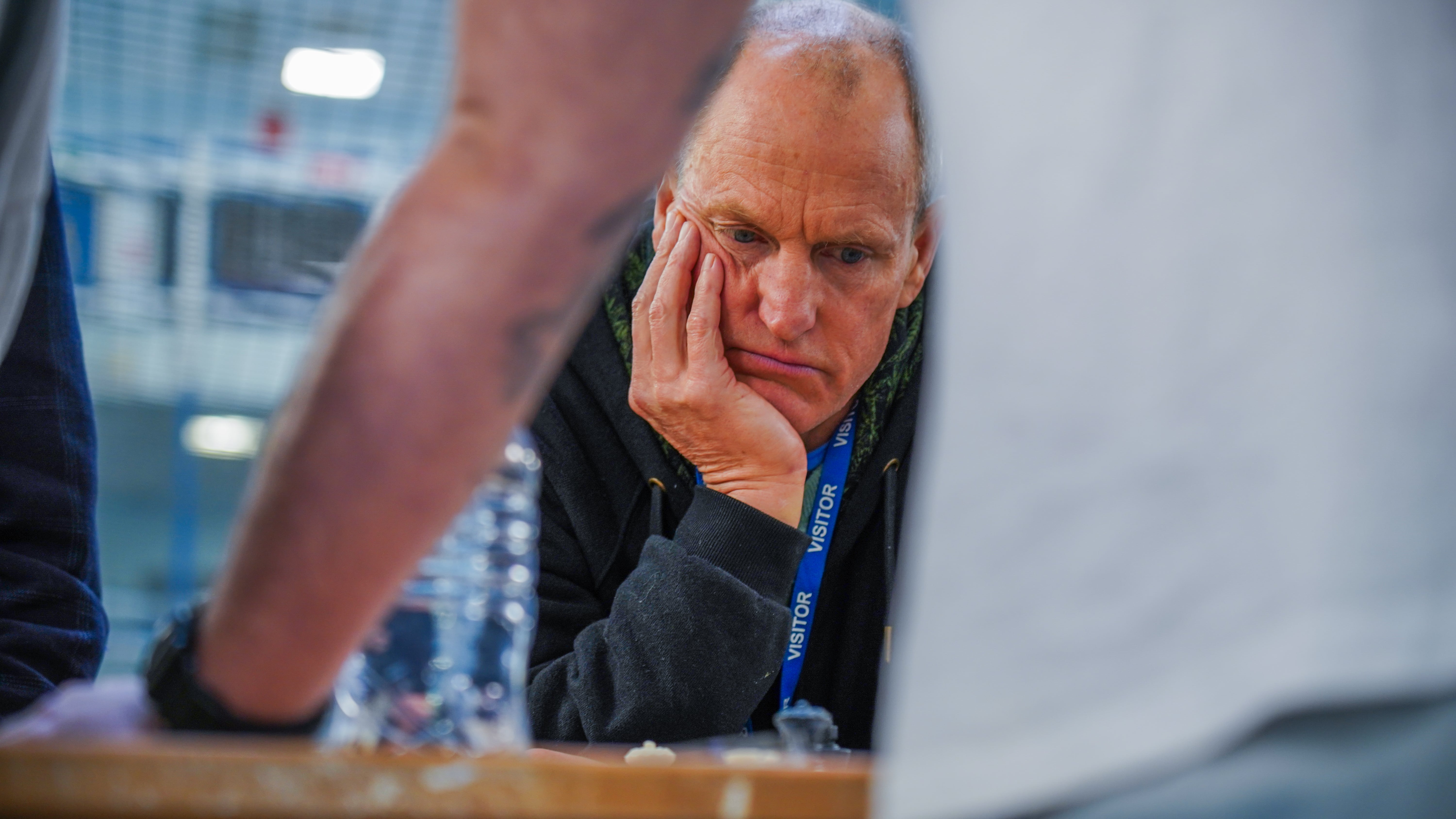 Actor Woody Harrelson holds his head in his hands while playing chess with a chess club in a prison