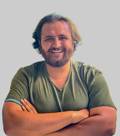 A young man in a white t-shirt stands against a light-colored background.