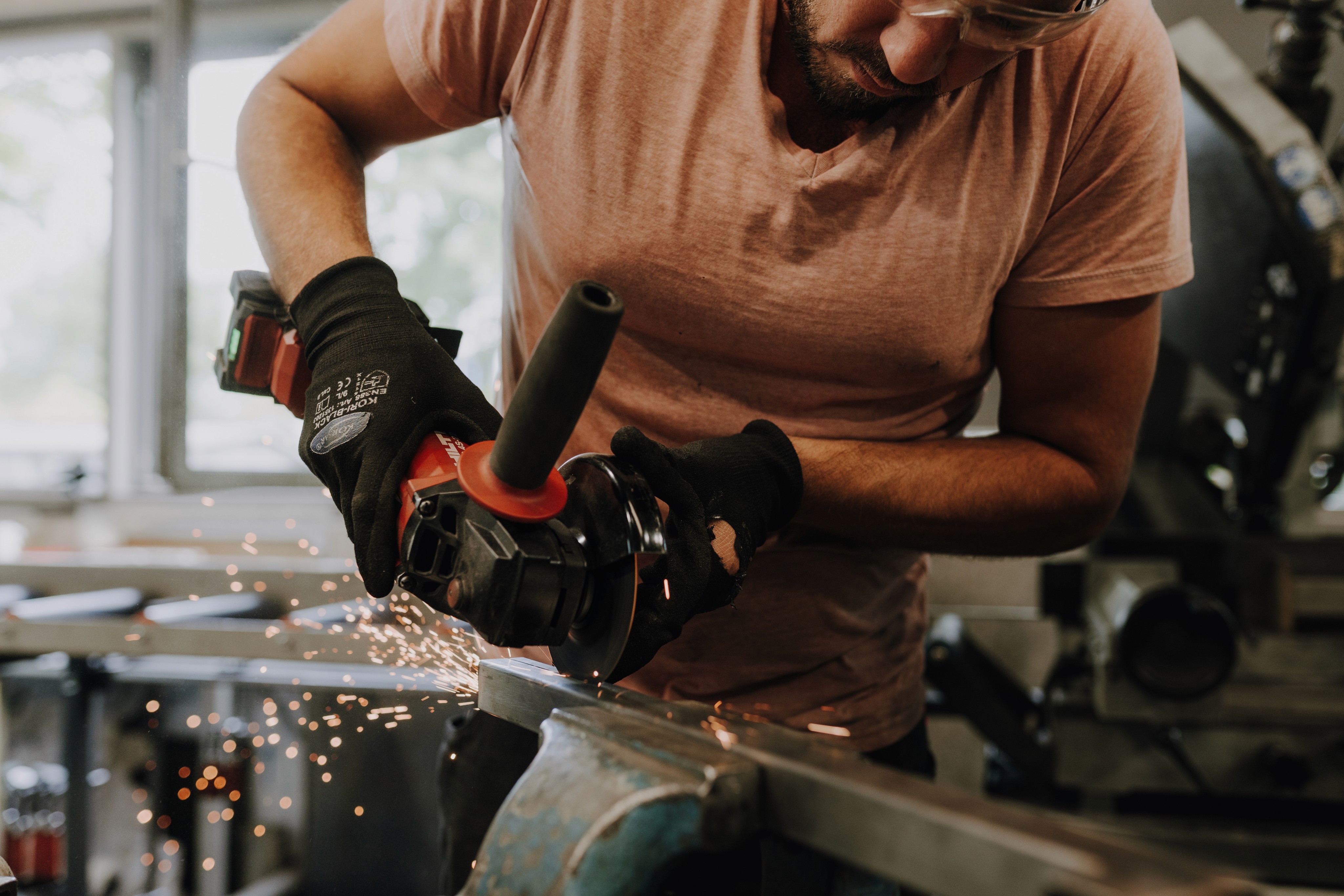 Man using a grinder, sparks flying, wearing safety glasses and black gloves, working with metal.