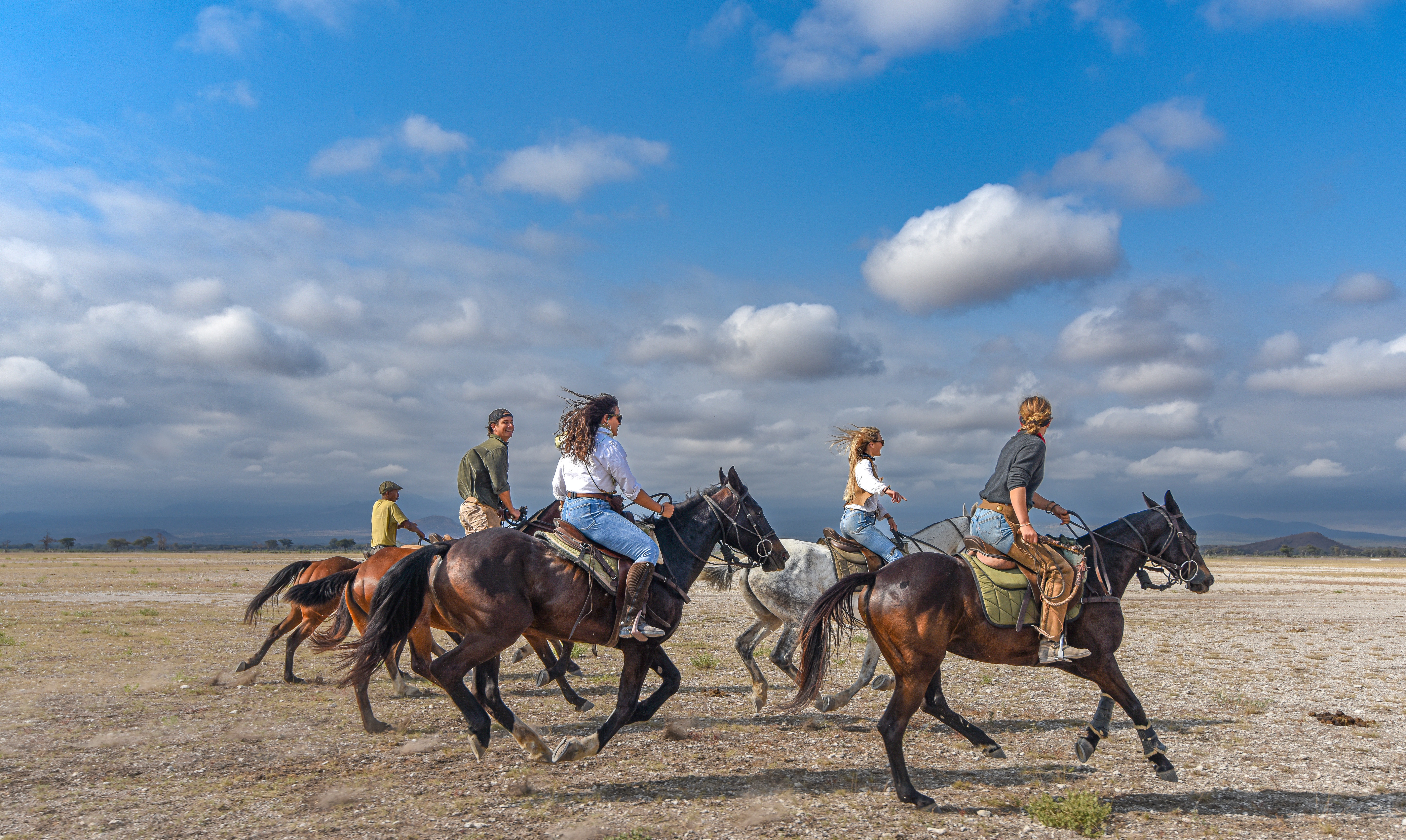 Kilimanjaro Elephant Ride, Arusha National Park, Tanzania – en grupp ryttare till häst galopperar över en öppen savann under blå himmel på ridsafari i Afrika.