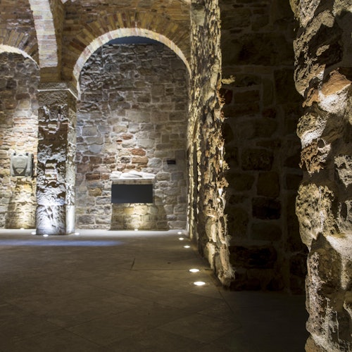 昏暗的石墙内饰,拱形天花板由地面射灯照明,特色是裸露的砖墙和富有质感的墙面。