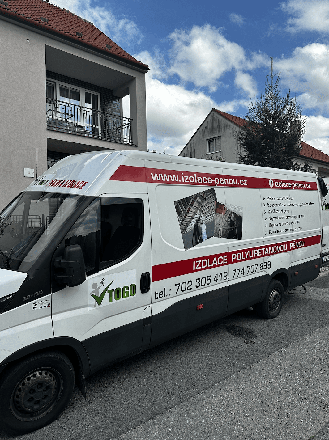 A smiling young man with crossed arms, wearing a plaid shirt and white t-shirt, poses against a dark background.