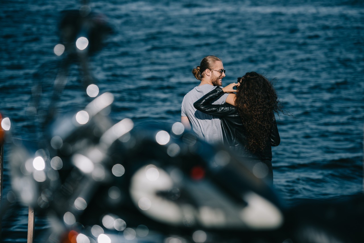 Two motorcyclists have disembarked to take a photo by the sea