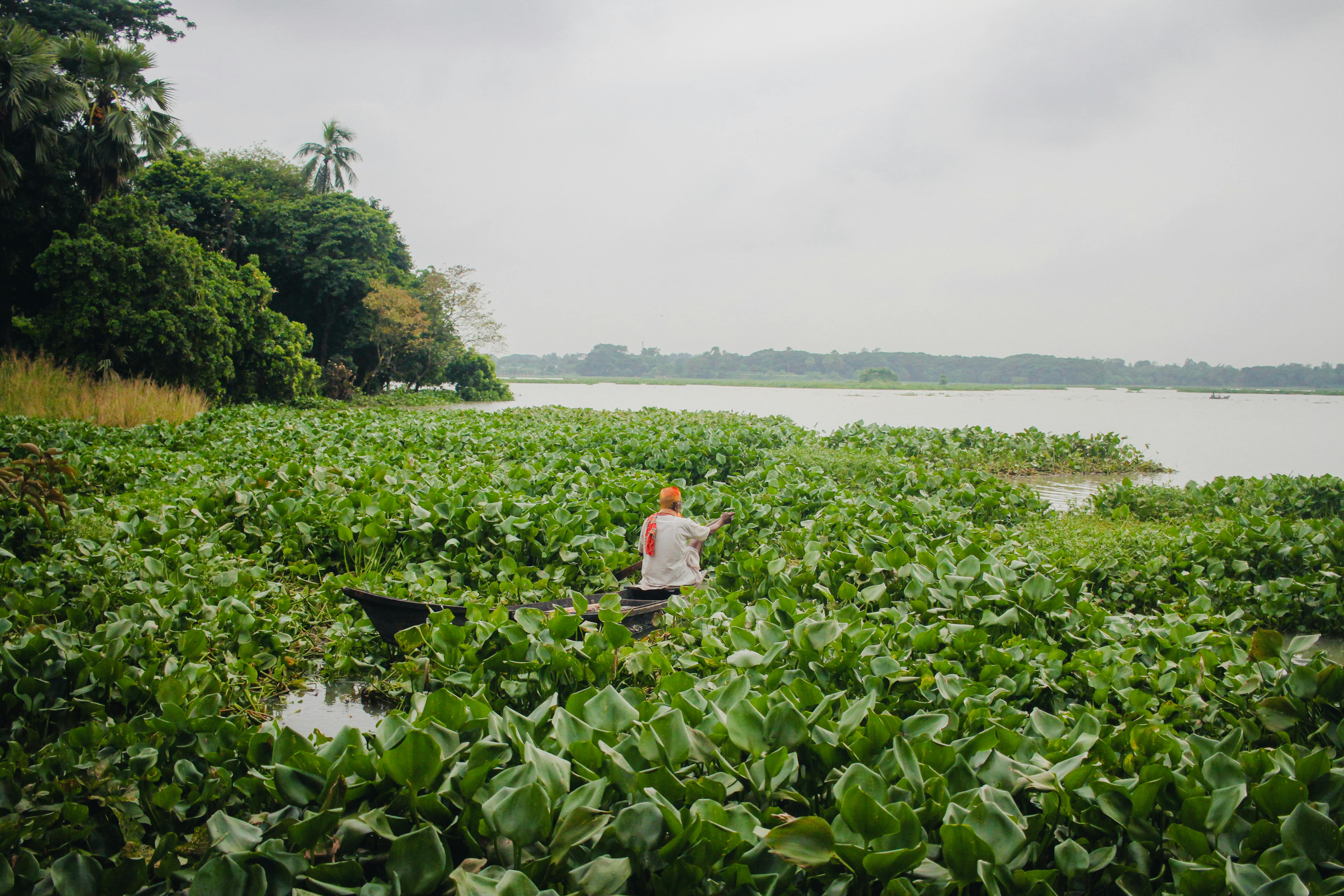 Smiling young woman with long hair standing against a dark green background, holding a finger to her chin.