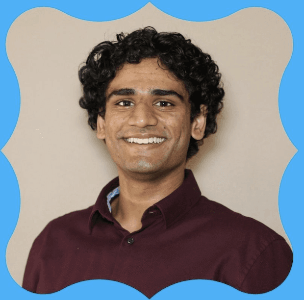 Saad smiling in front of a brown background
