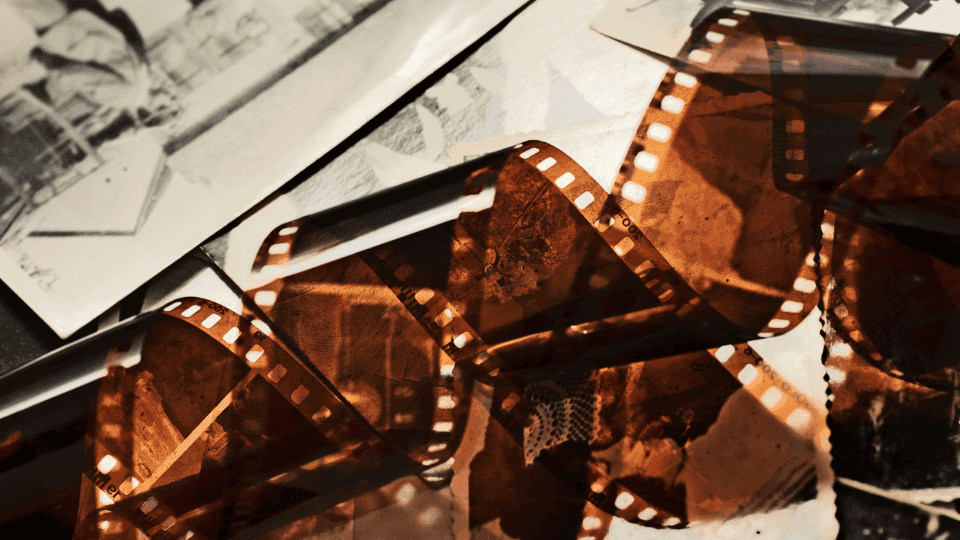 Strips of developed film negatives scattered over old black and white photographs, lit with warm amber tones.